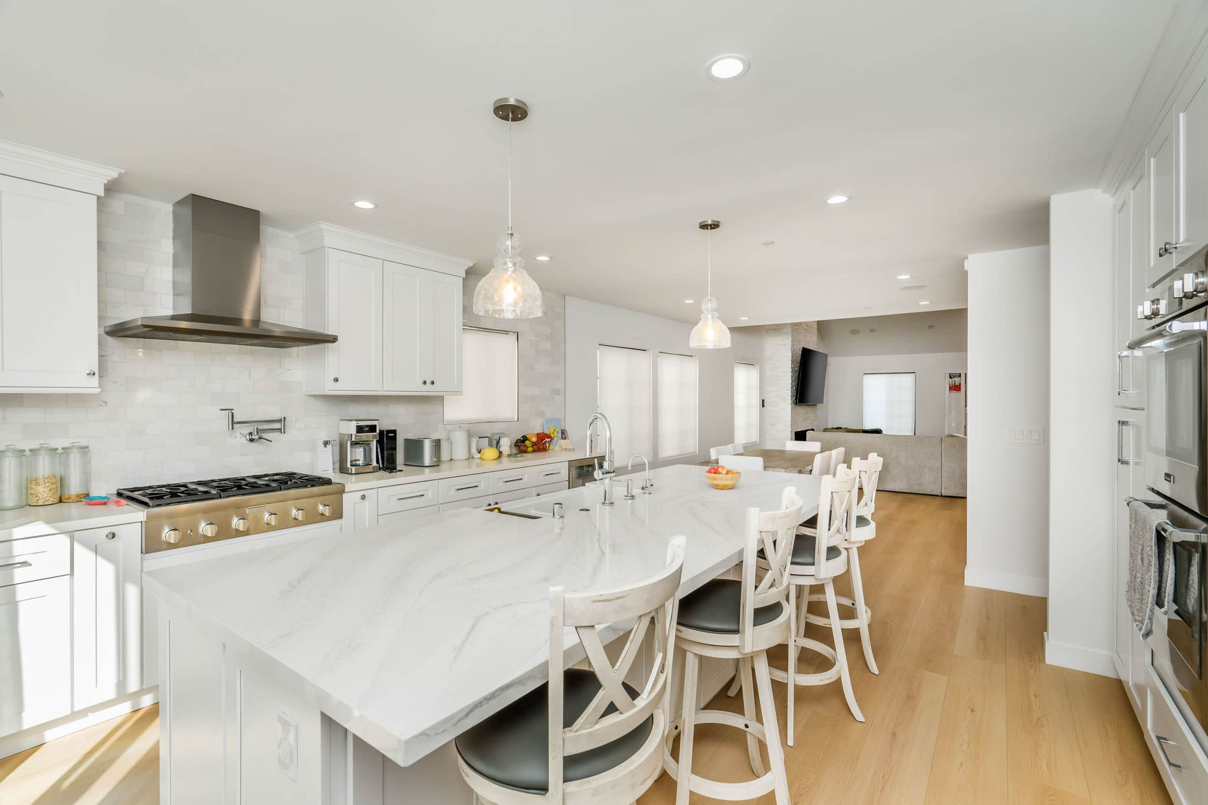 The image shows a modern kitchen with white cabinetry, a large island with seating, and stainless steel appliances.