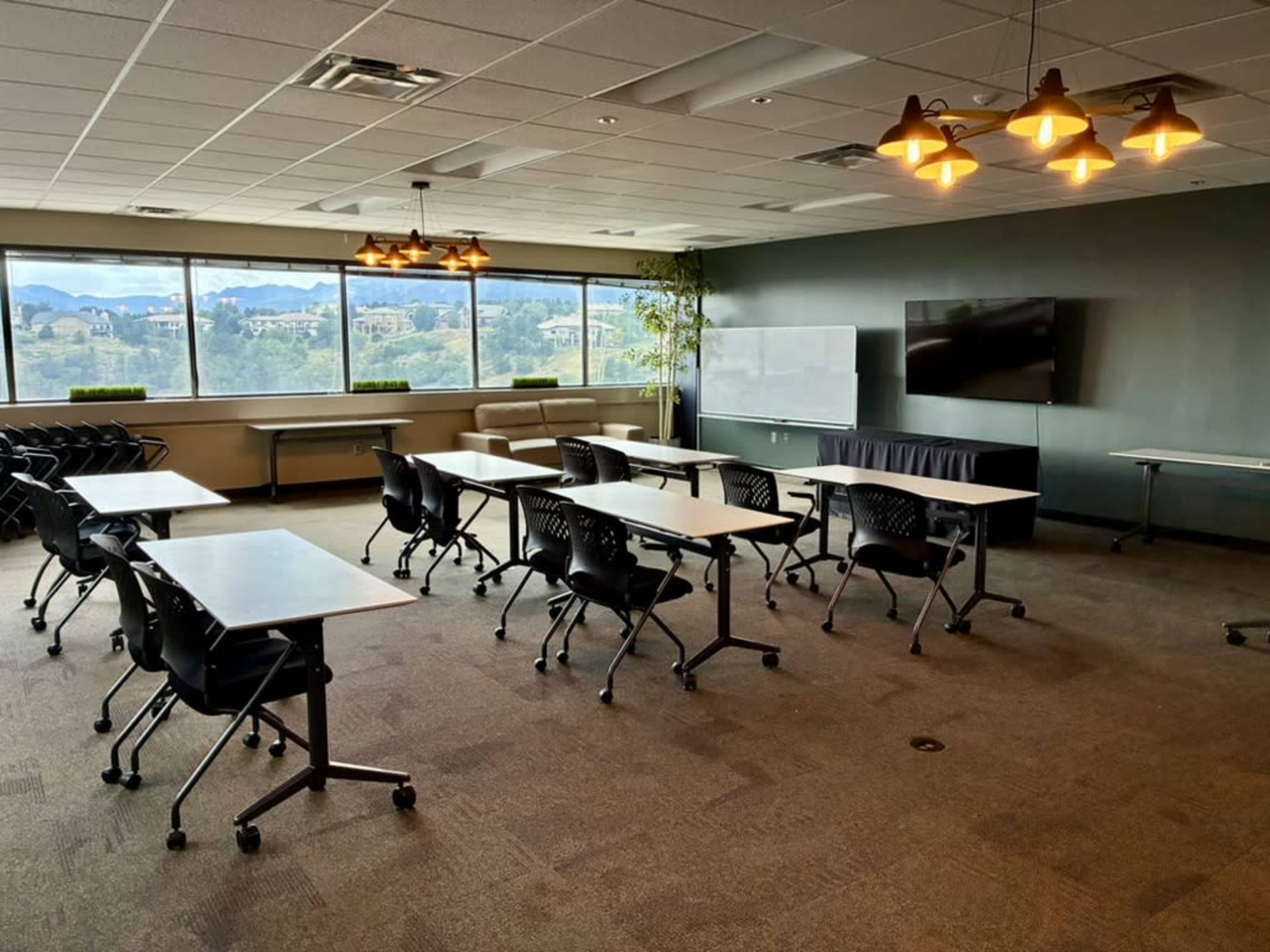 A conference room with multiple tables and chairs arranged for a meeting, featuring large windows overlooking a mountainous landscape.