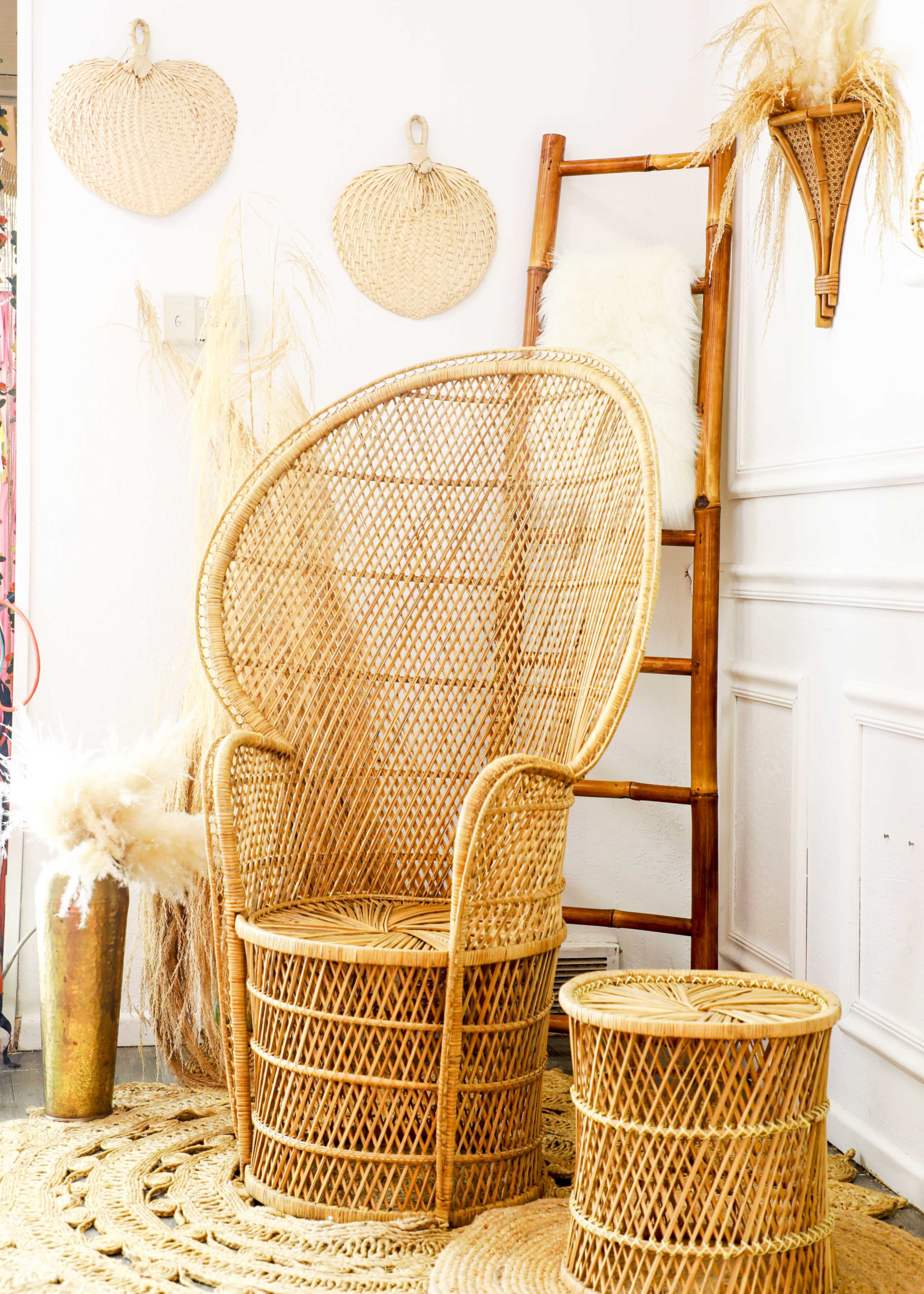 The image features a wicker chair and a round side table, both set against a light-colored wall adorned with woven decor and a bamboo ladder.