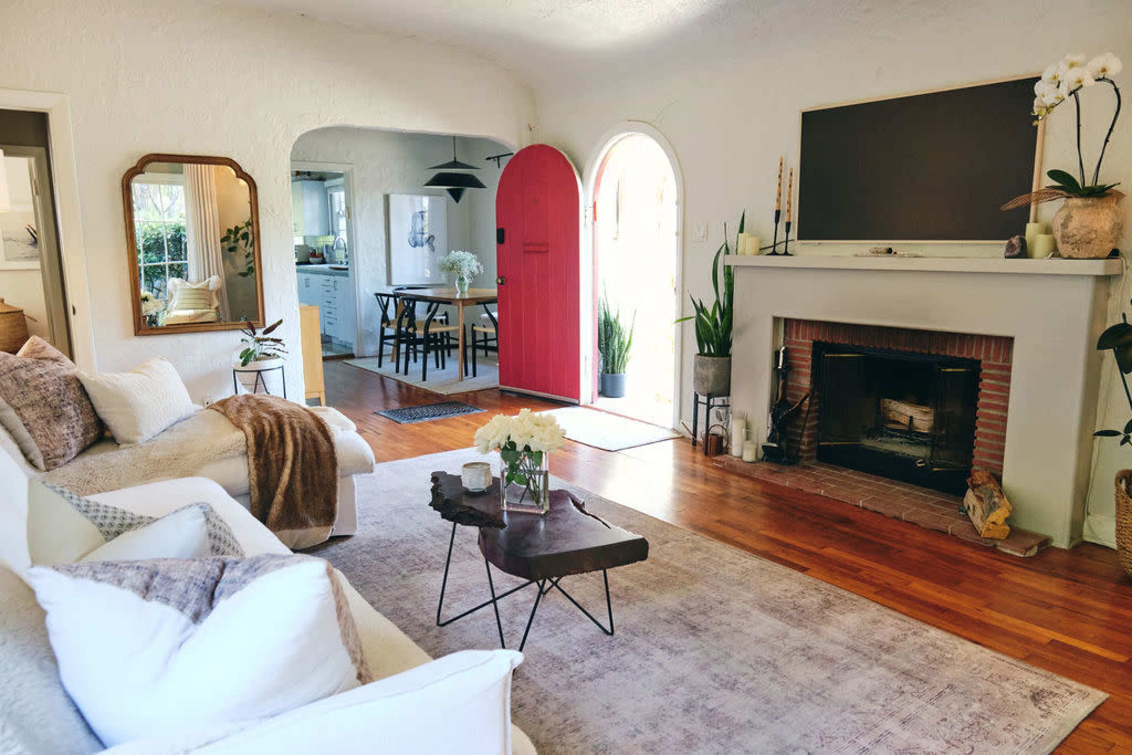The image shows a cozy living room featuring a white sofa, a wooden coffee table, and a fireplace, with a bright pink door leading to another space.