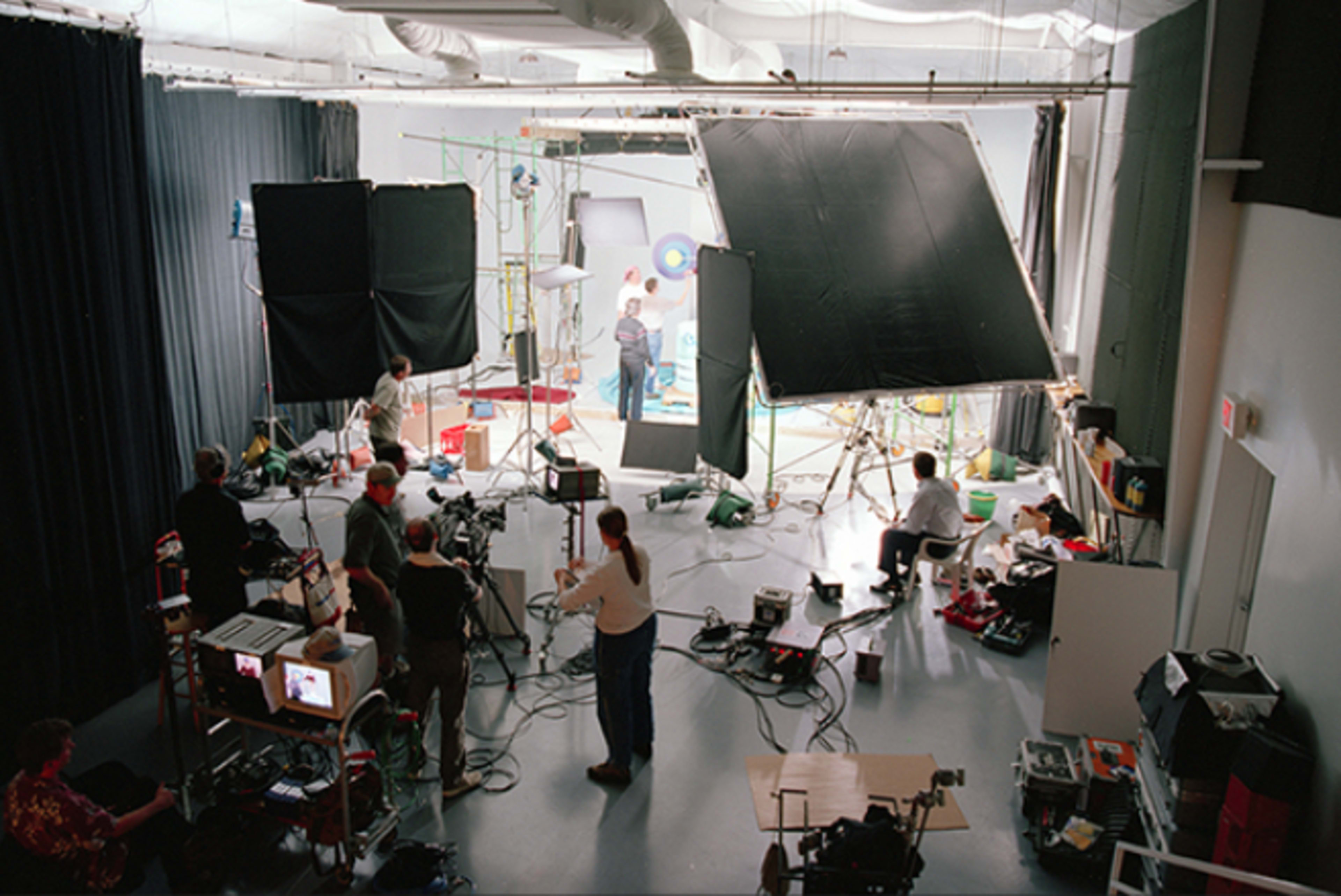 A photography studio is set up with multiple lights, cameras, and crew members working on a shoot.