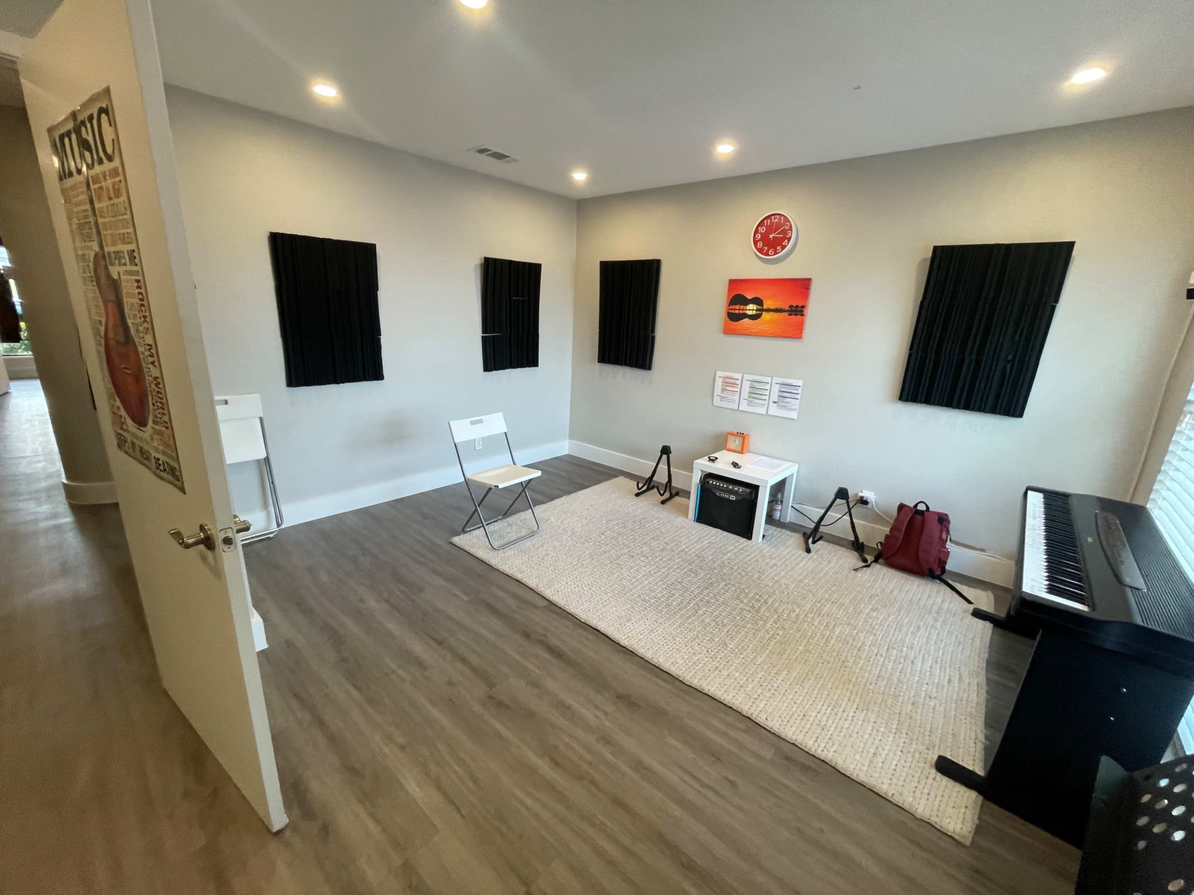 A music practice room with black soundproof panels on the walls, a keyboard, chairs, and posters.