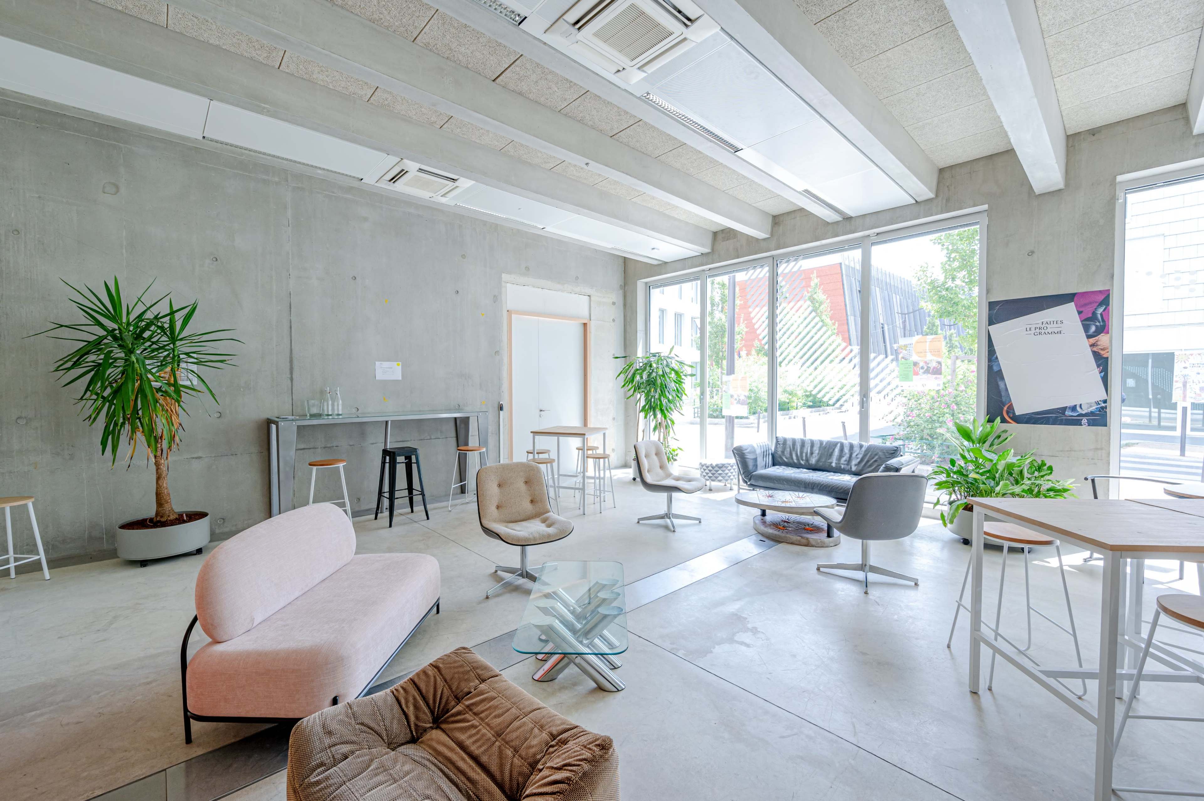 A modern lounge area with concrete walls, various seating arrangements, and large windows that let in natural light.