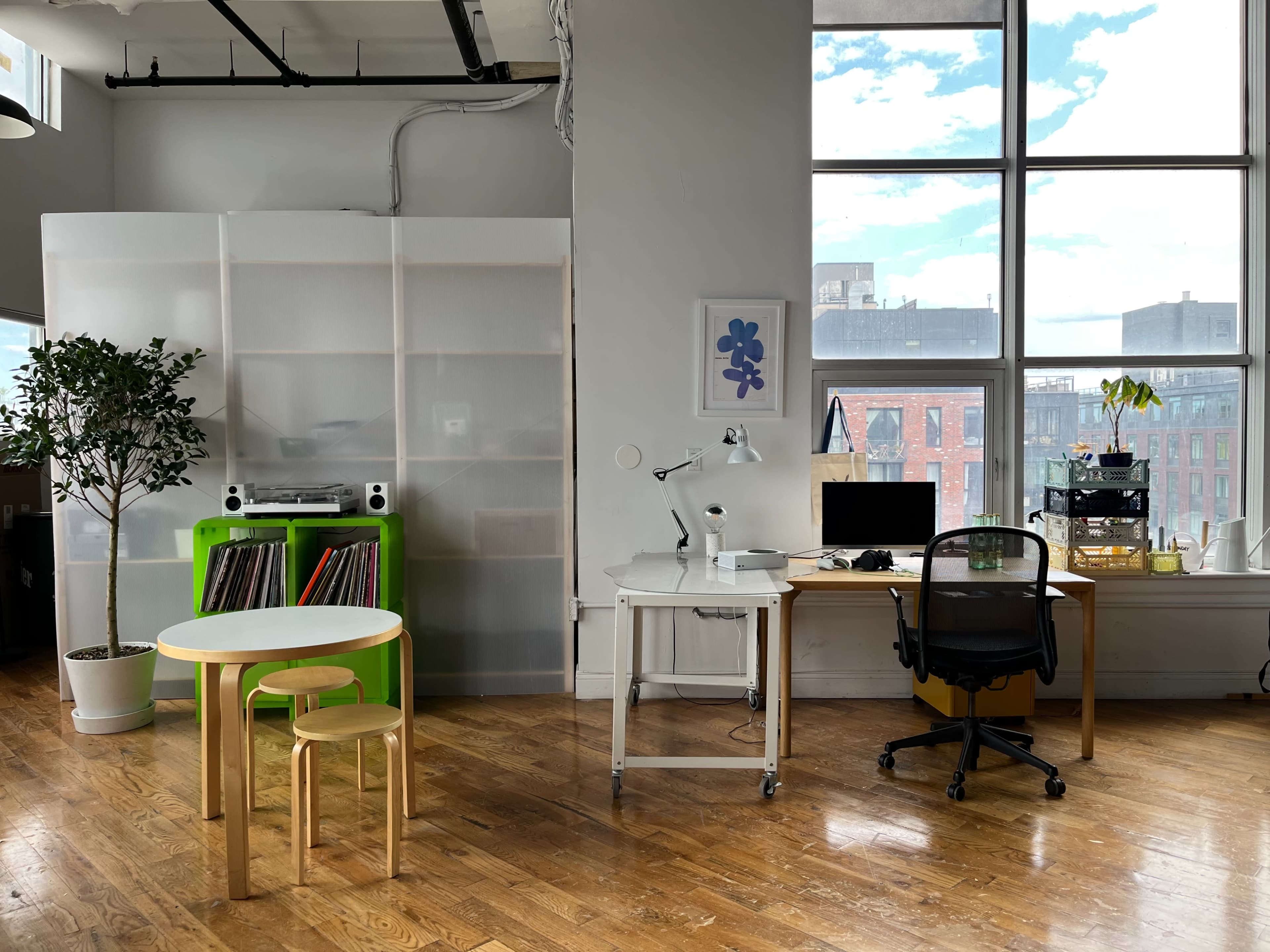 A bright, modern office interior with two workspaces, a small table, and a plant, separated by a translucent partition.