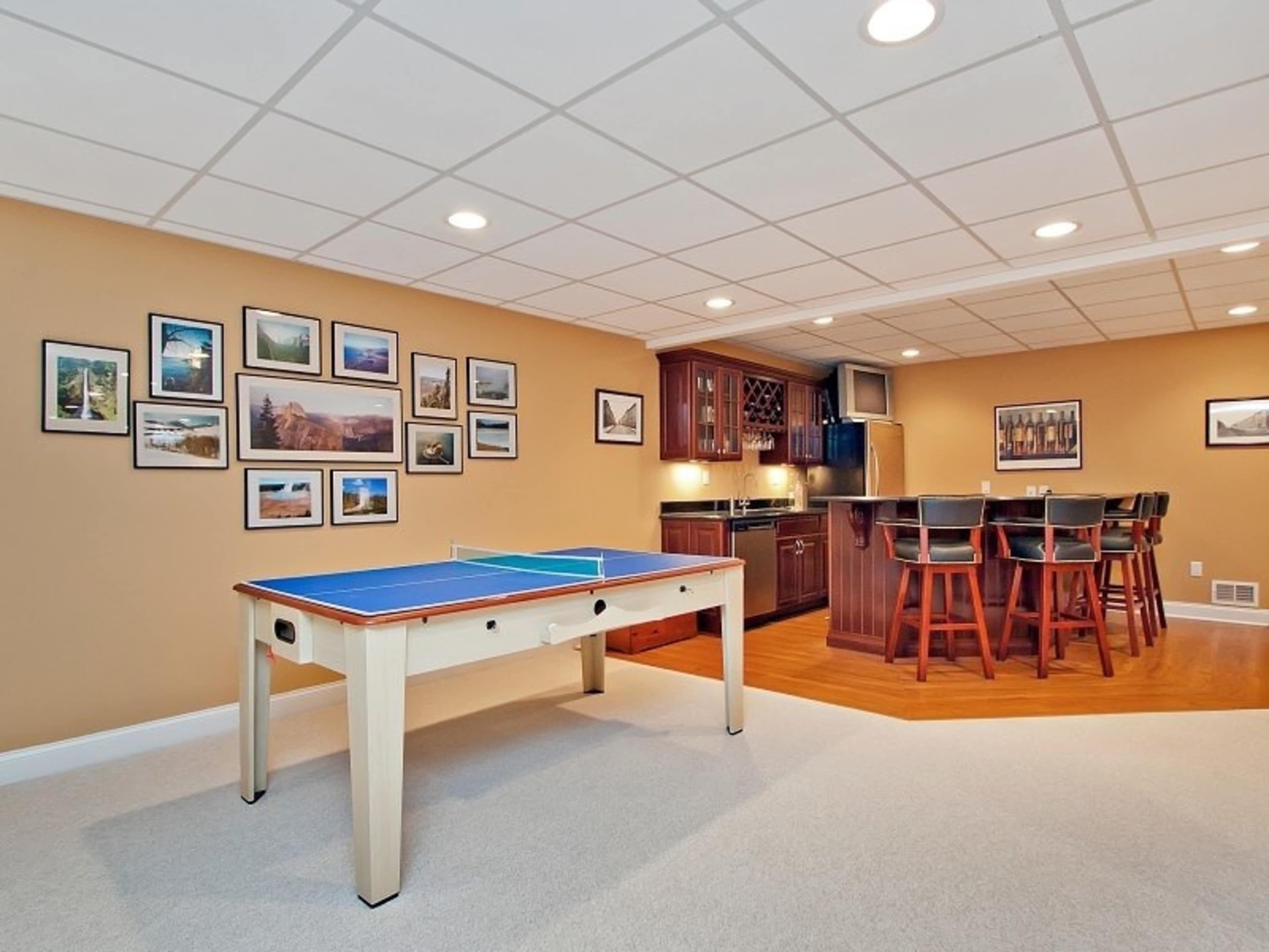 A finished basement with a ping pong table, a bar area with high stools, and framed pictures on the walls.