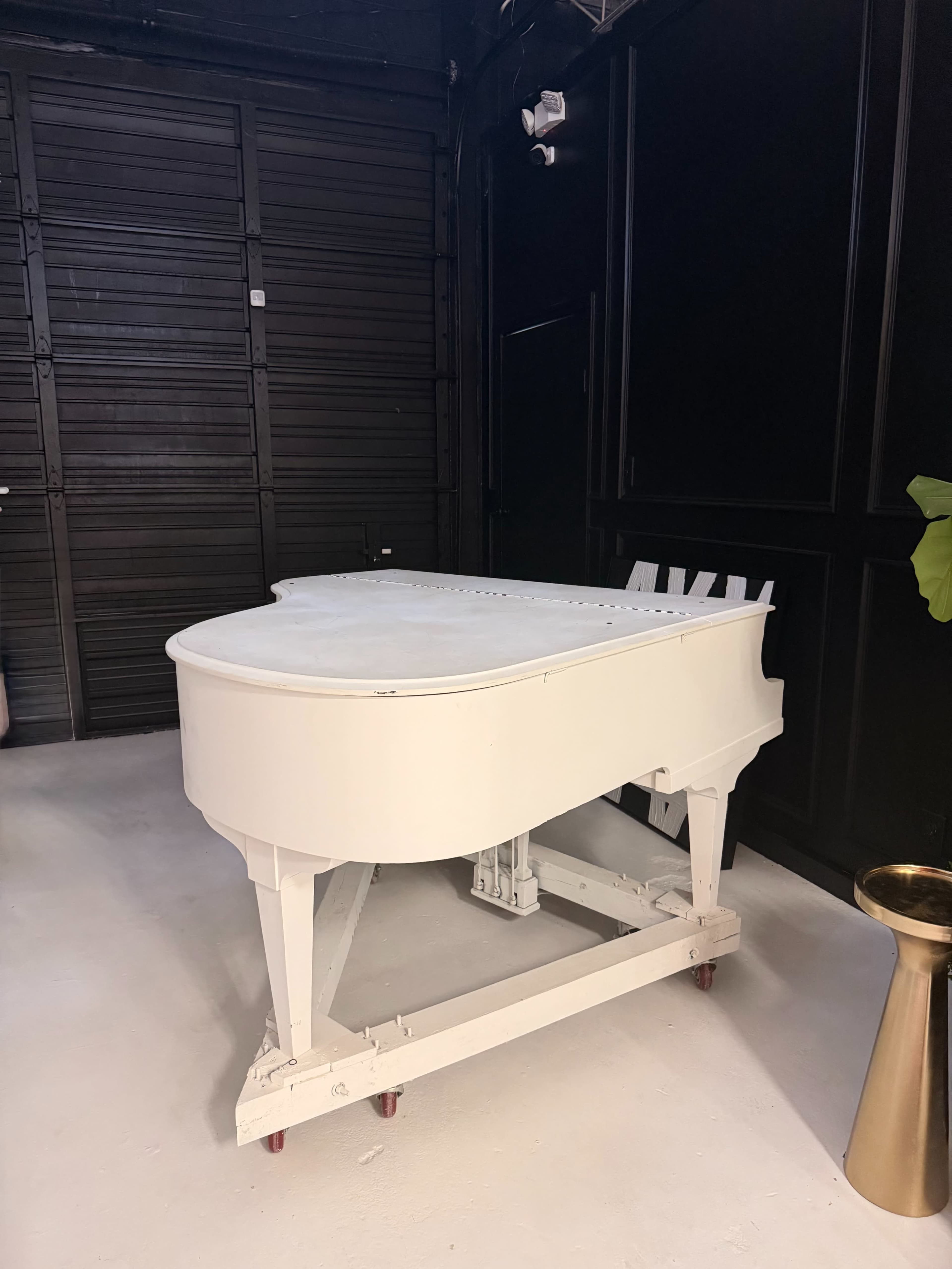 A white grand piano on wheels is positioned against a dark wall in a spacious room.
