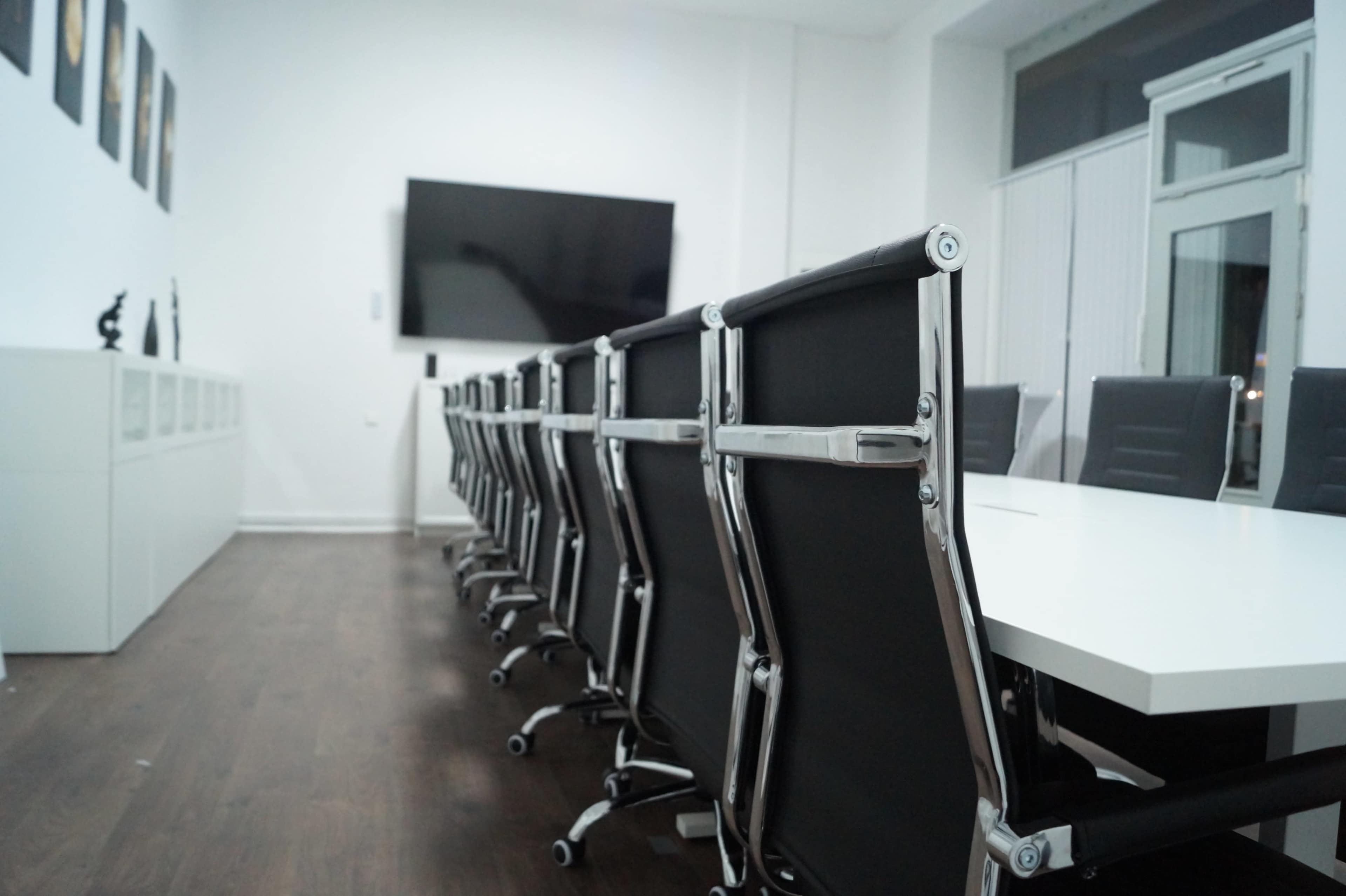 A modern conference room features a long table with black ergonomic chairs and a large wall-mounted display screen.