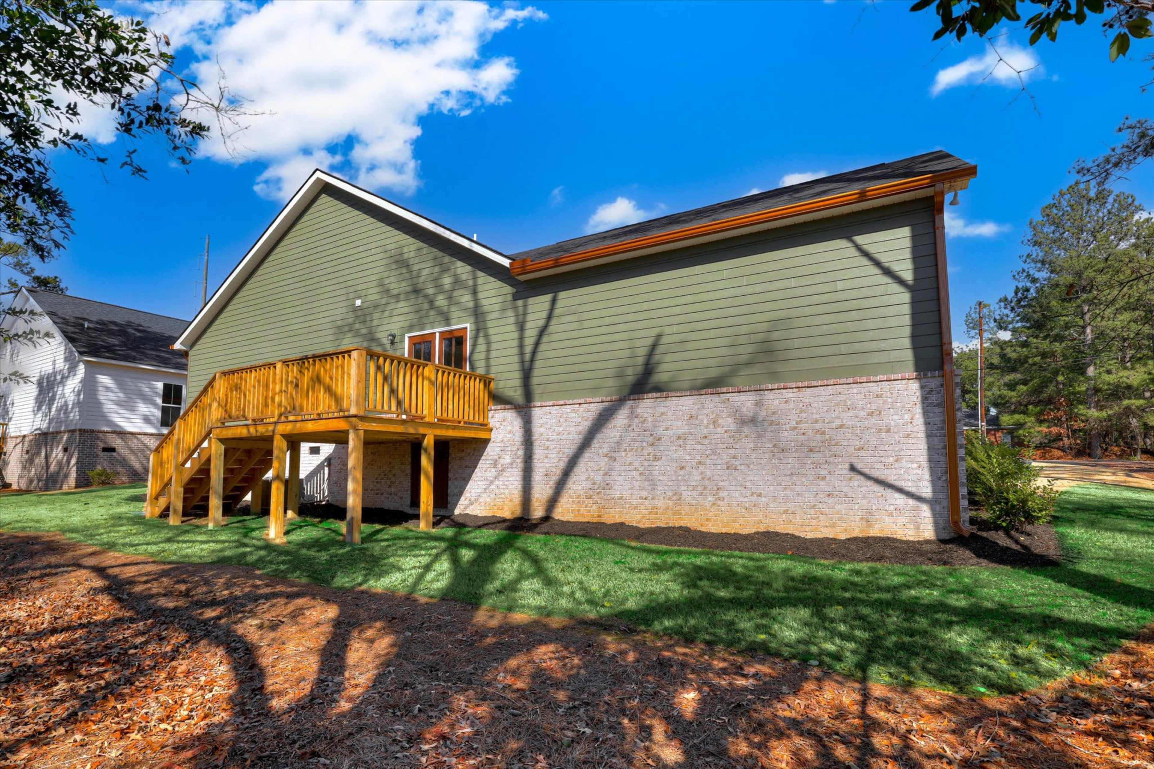 The image shows a green house with a wooden deck on the side, surrounded by a well-maintained lawn and trees.