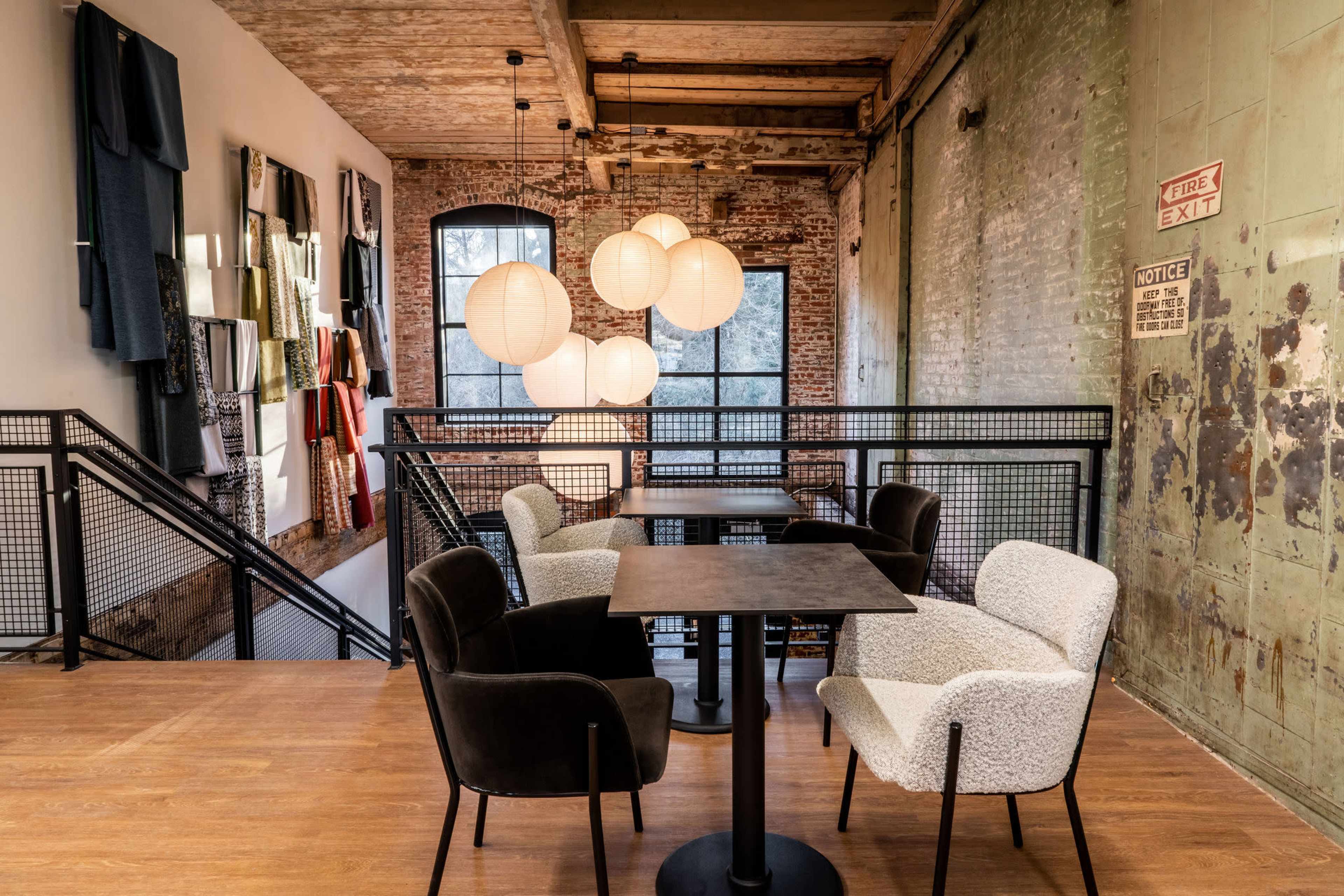 A cozy seating area with four chairs and a table, illuminated by round pendant lights, located in a space featuring exposed brick and a rustic design.