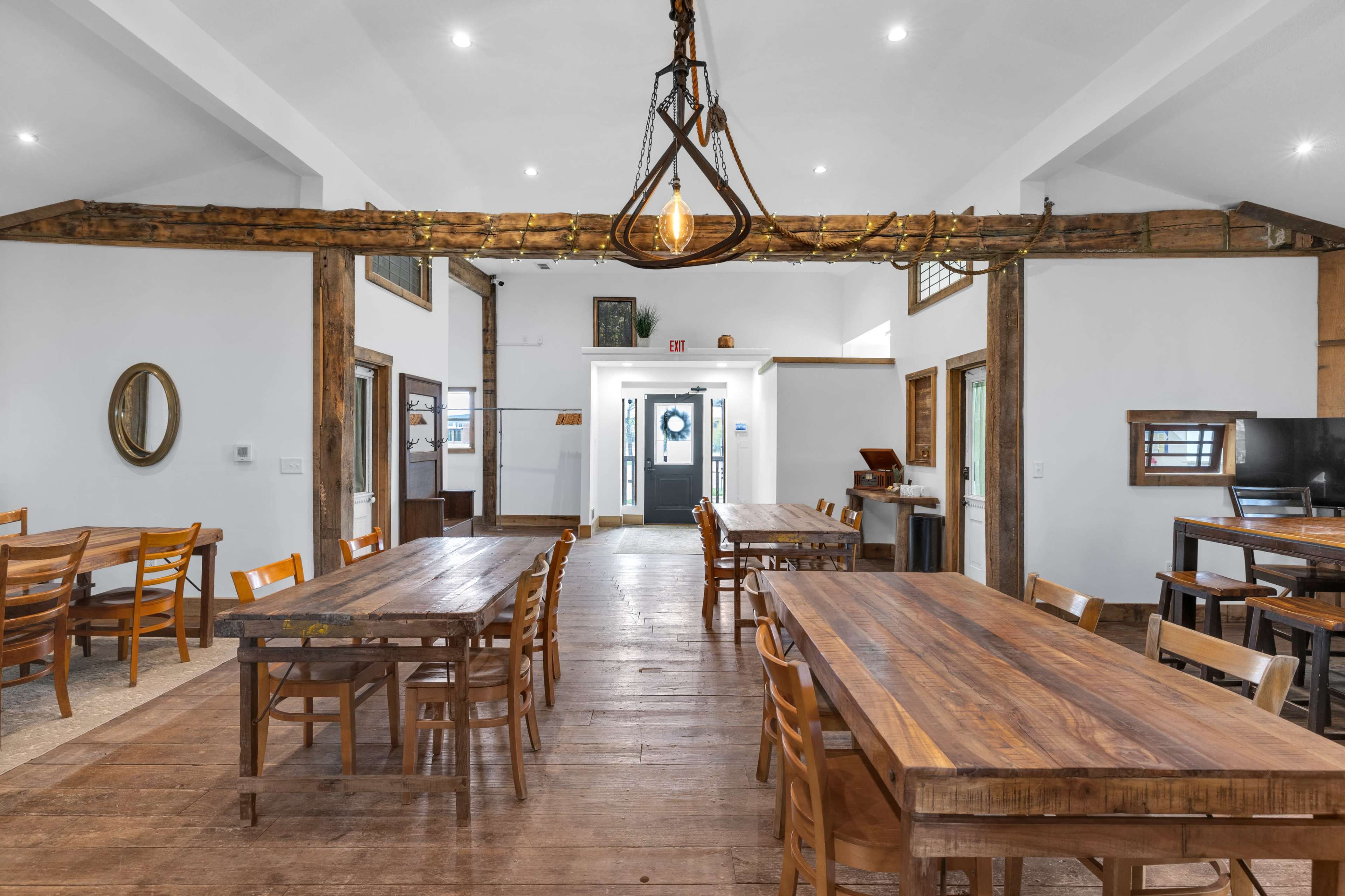 The image shows a spacious dining area with wooden tables and chairs, illuminated by a decorative light fixture hanging from a wooden beam.