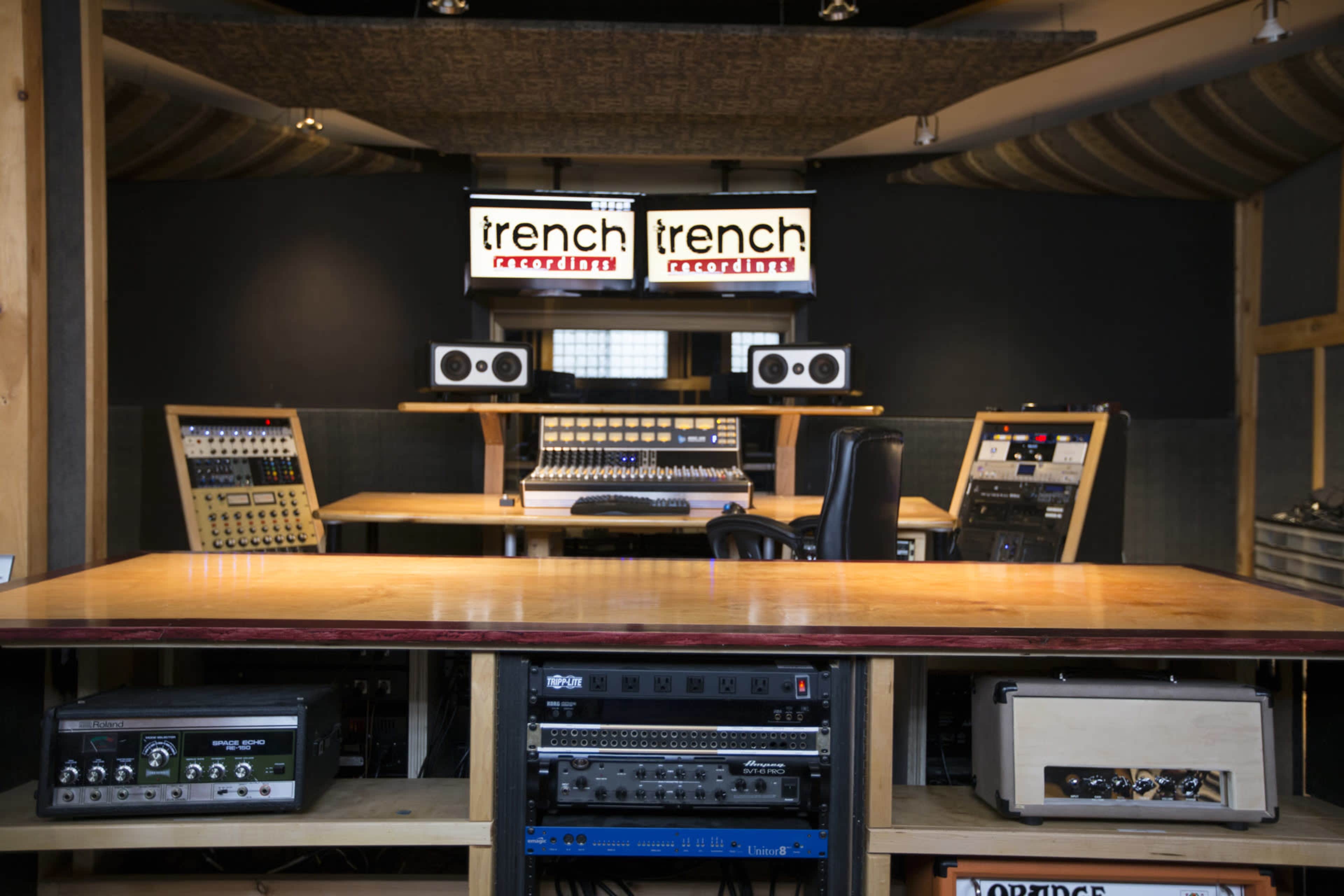 A sound recording studio with a central mixing console, speakers, and various audio equipment arranged on a wooden surface.