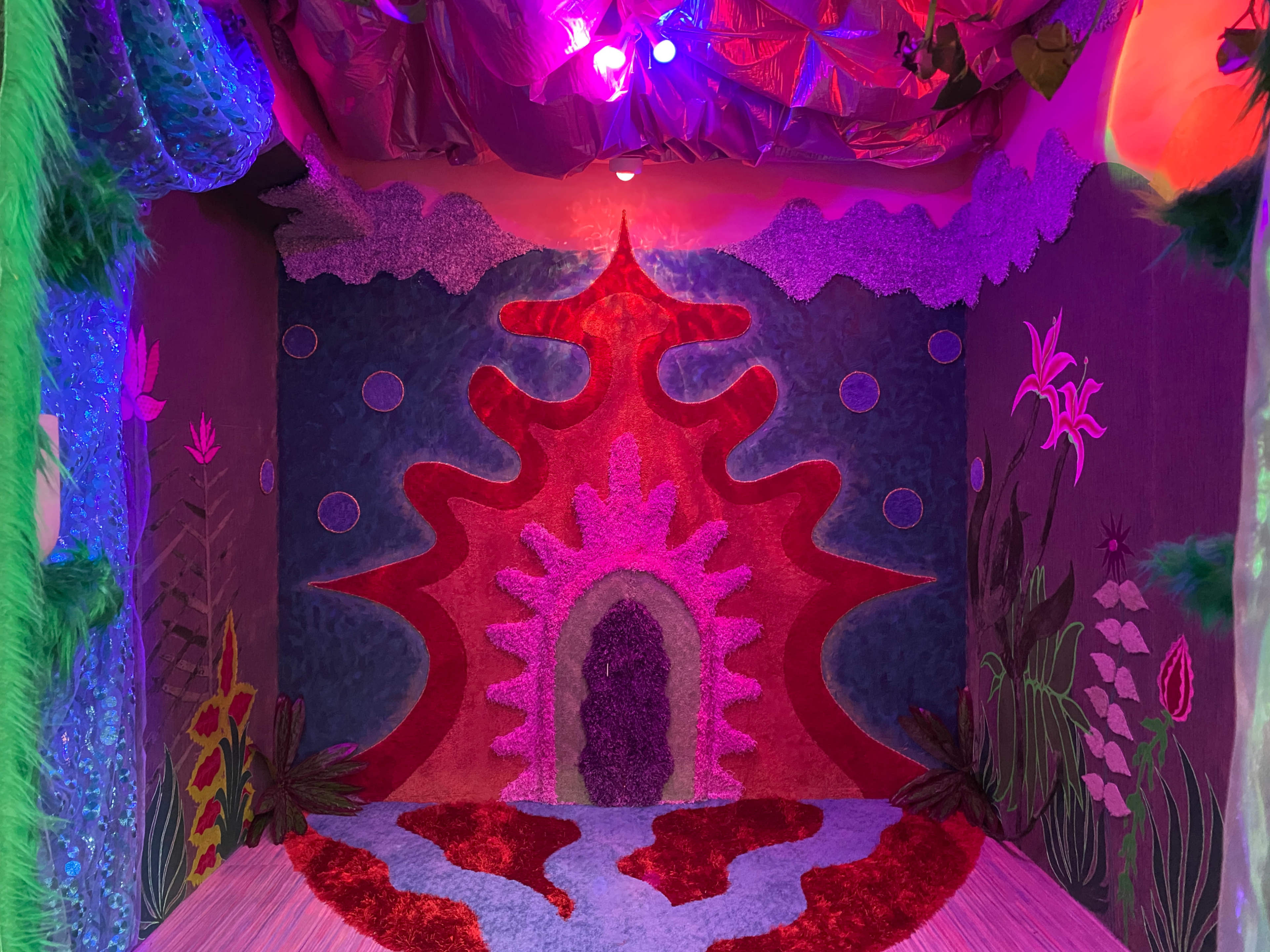 The image shows a vibrant interior space decorated with colorful, textured walls featuring abstract designs and plant motifs.