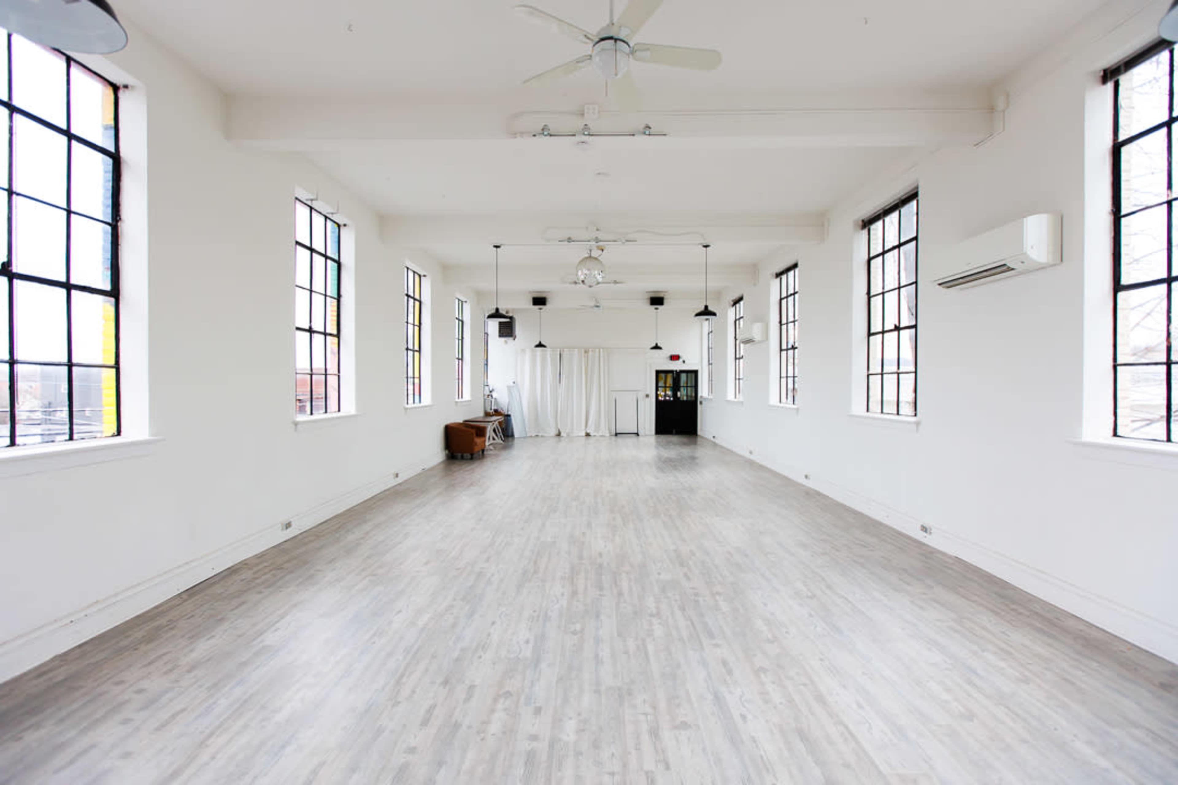 A spacious, airy interior with large windows, light wooden flooring, and minimal furniture.