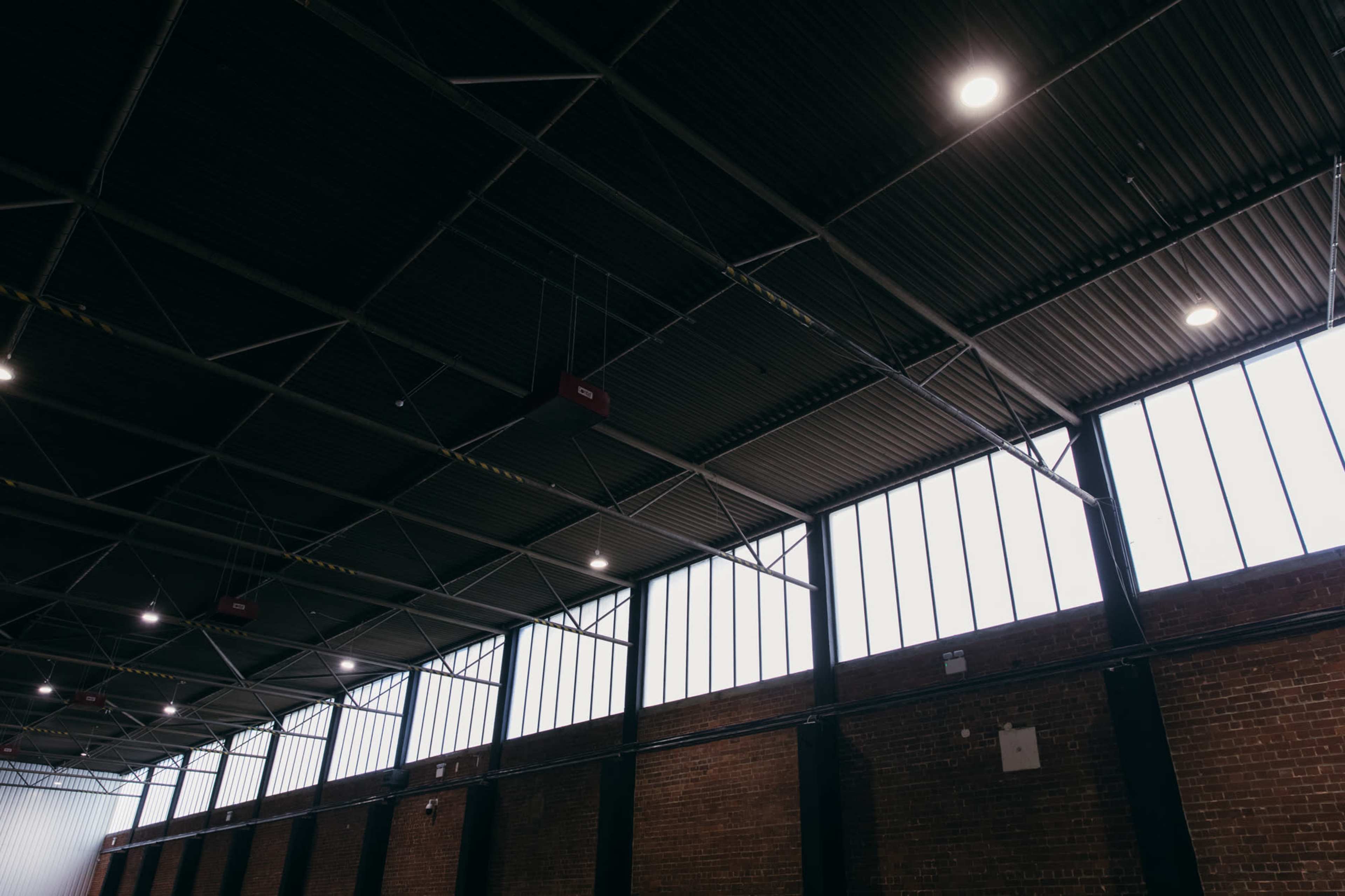 The interior of a large industrial space with a metal ceiling and tall windows allowing natural light to enter.