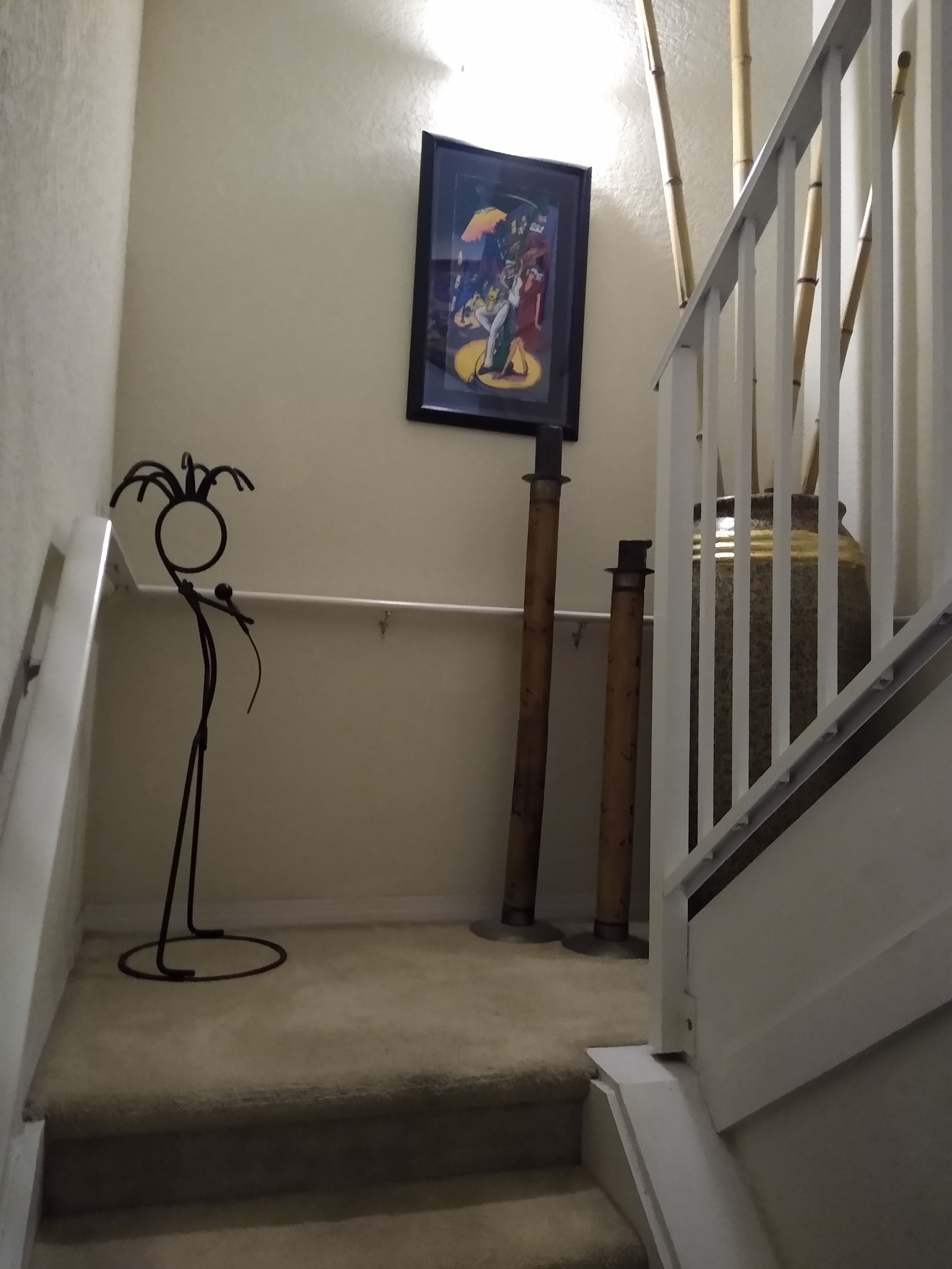 A stairway with a beige carpet, a framed picture on the wall, tall bamboo plants, and decorative objects placed along the stairs.