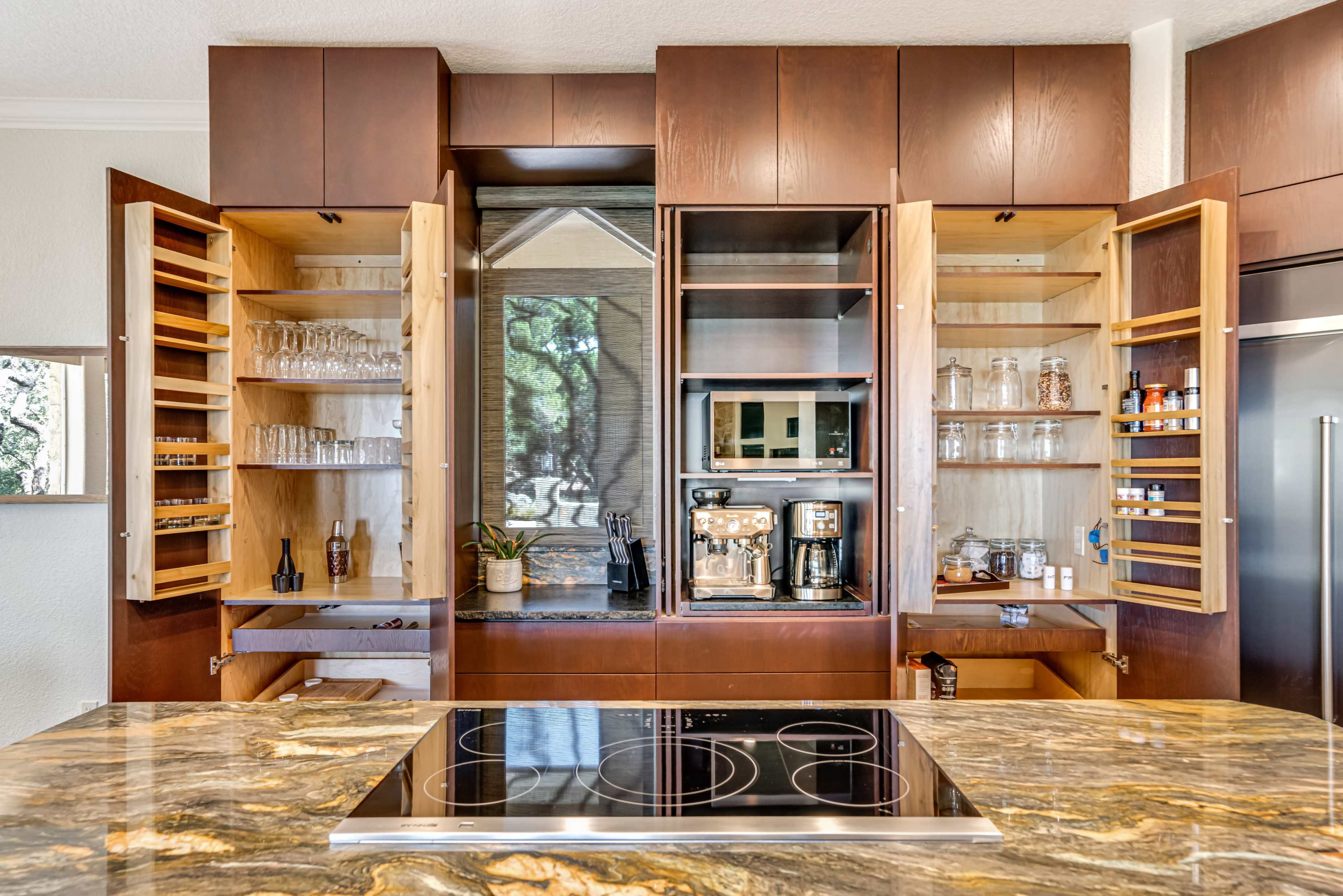 A modern kitchen with open cabinetry revealing shelves of glassware and coffee equipment, and a central cooking island with a built-in stovetop.