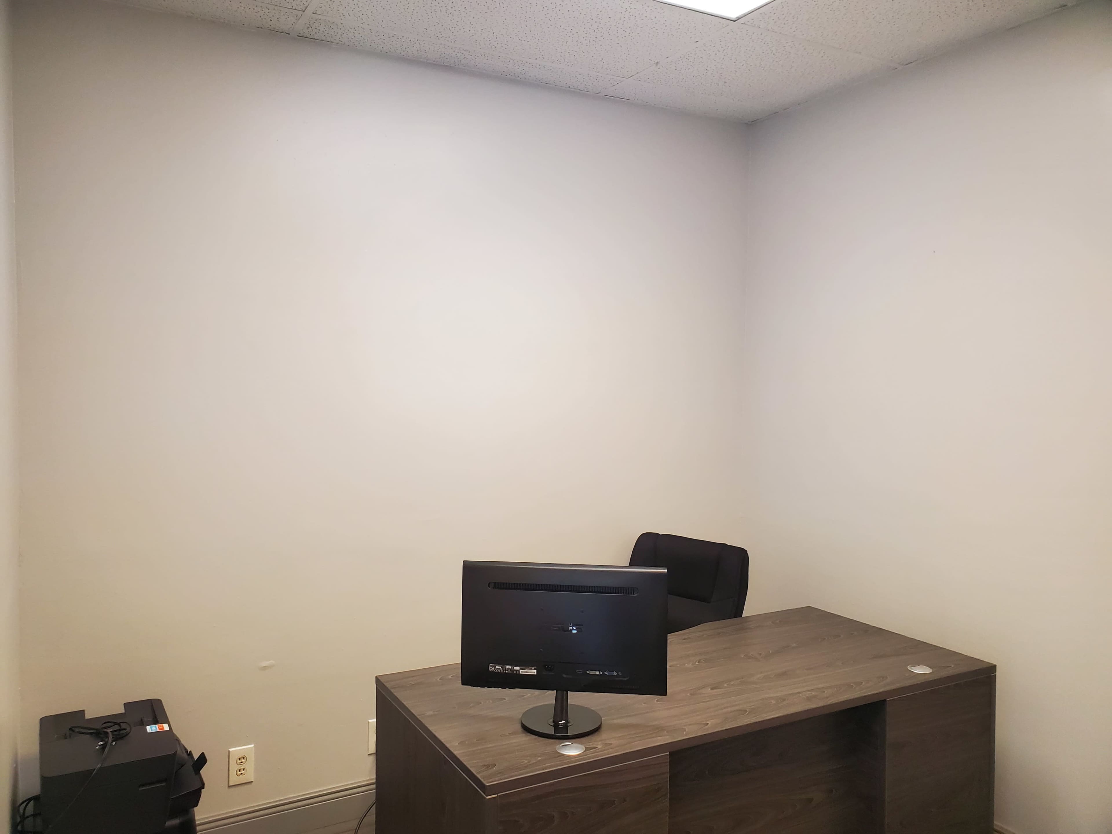 A sparse office space with a desk, a chair, and a monitor against a plain wall.