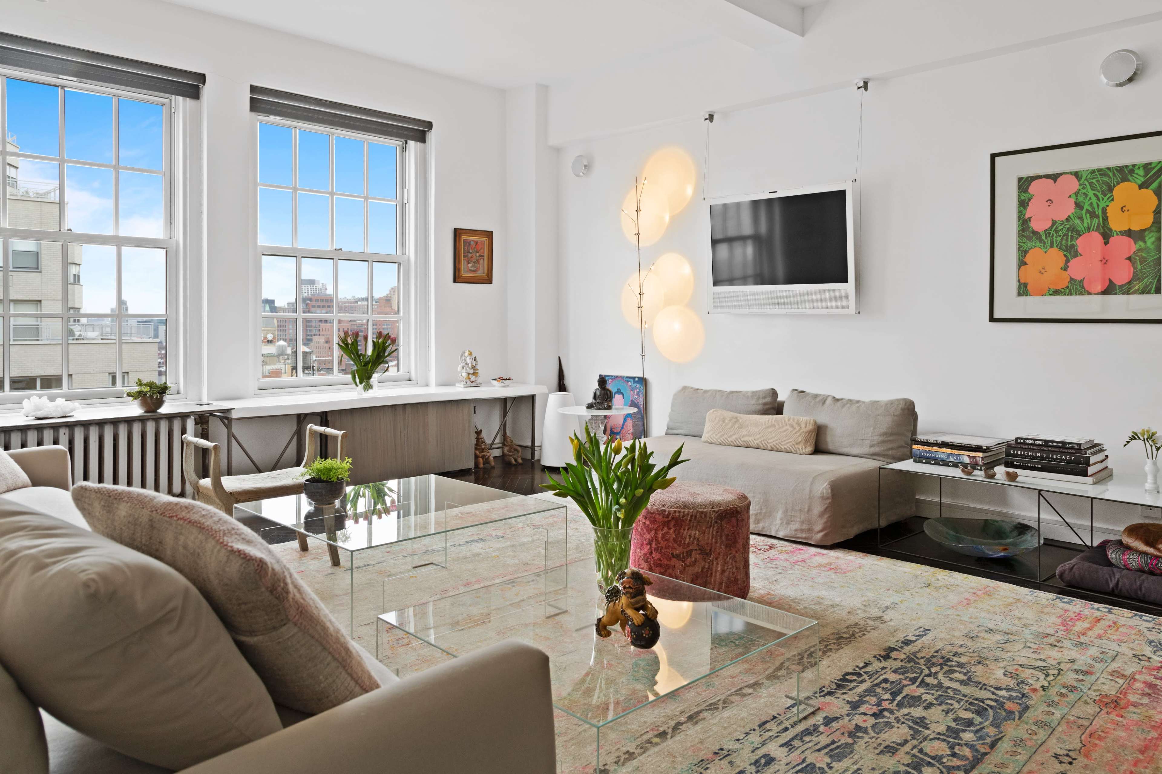 A modern living room features large windows, a glass coffee table, a sectional sofa, and decorative plants.