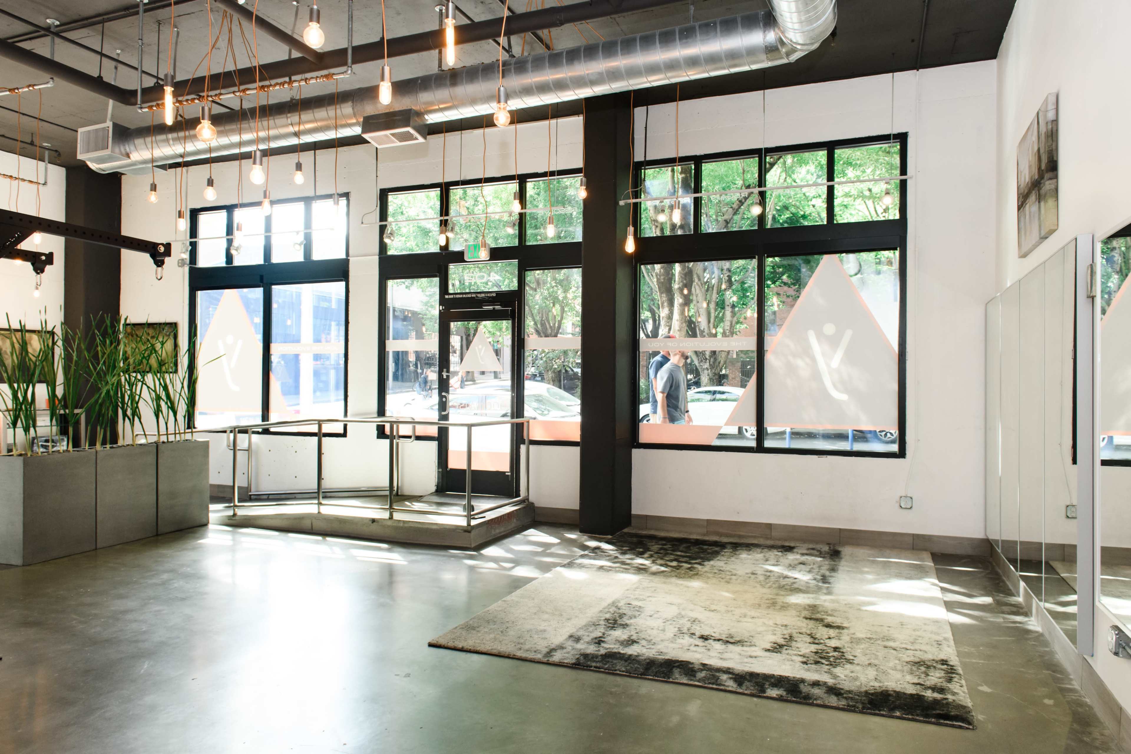 A spacious interior features large windows, pendant lights, and a minimalistic reception area with a rug and potted plants.