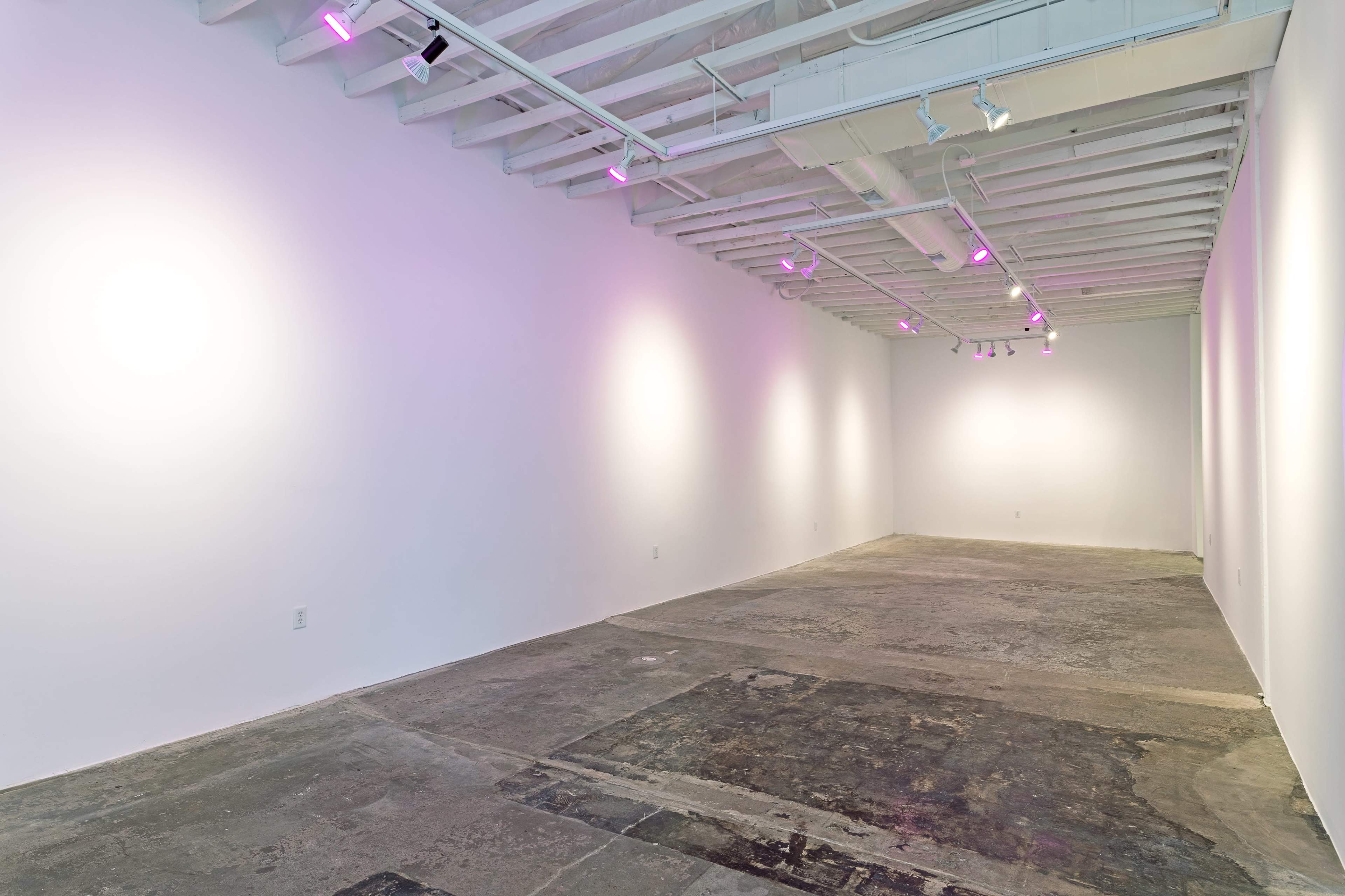 A minimalistic, empty art gallery with pink lighting and exposed beams.