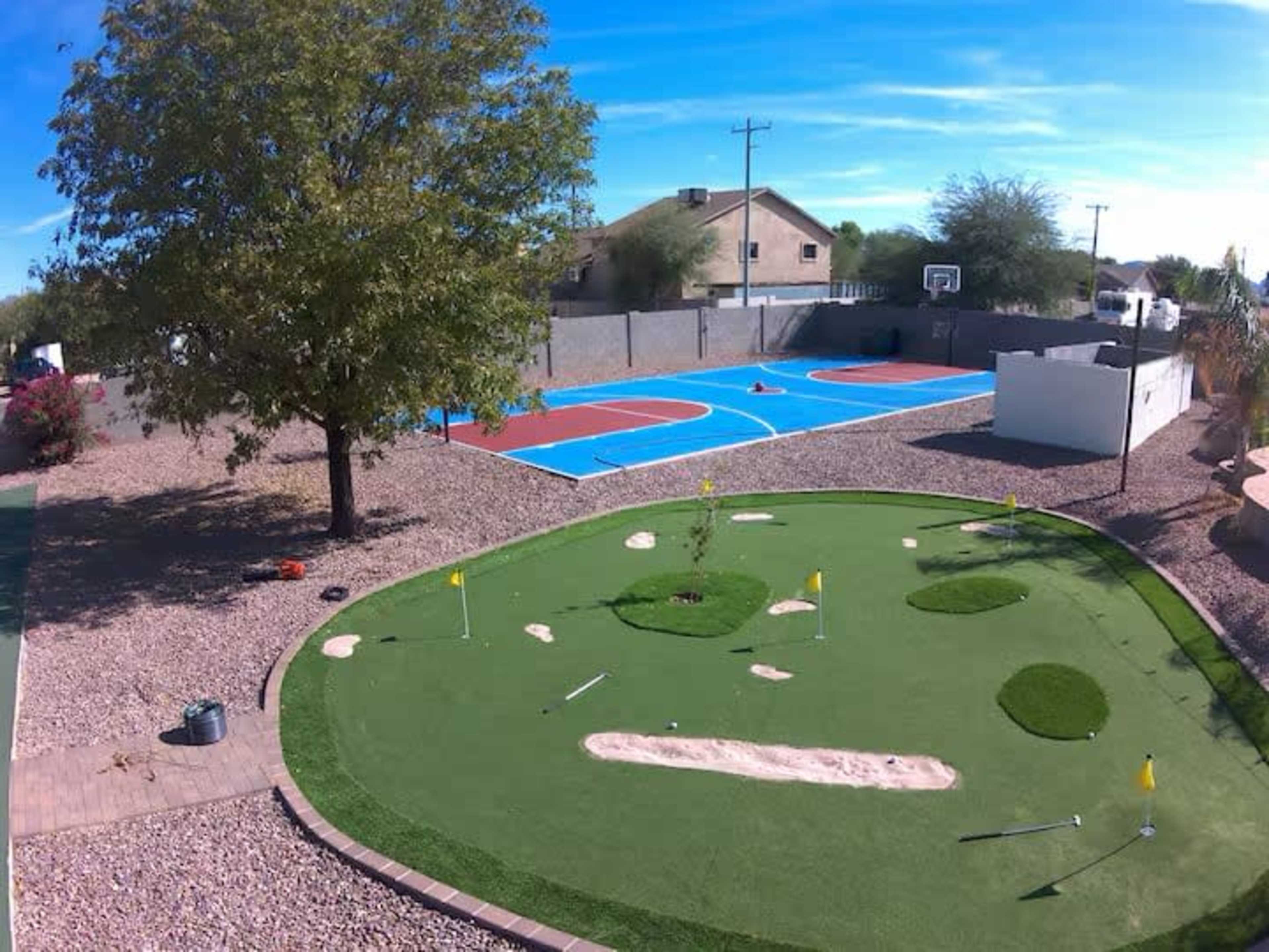 The image shows a backyard featuring a miniature golf course with flags, a basketball court, and a large tree.