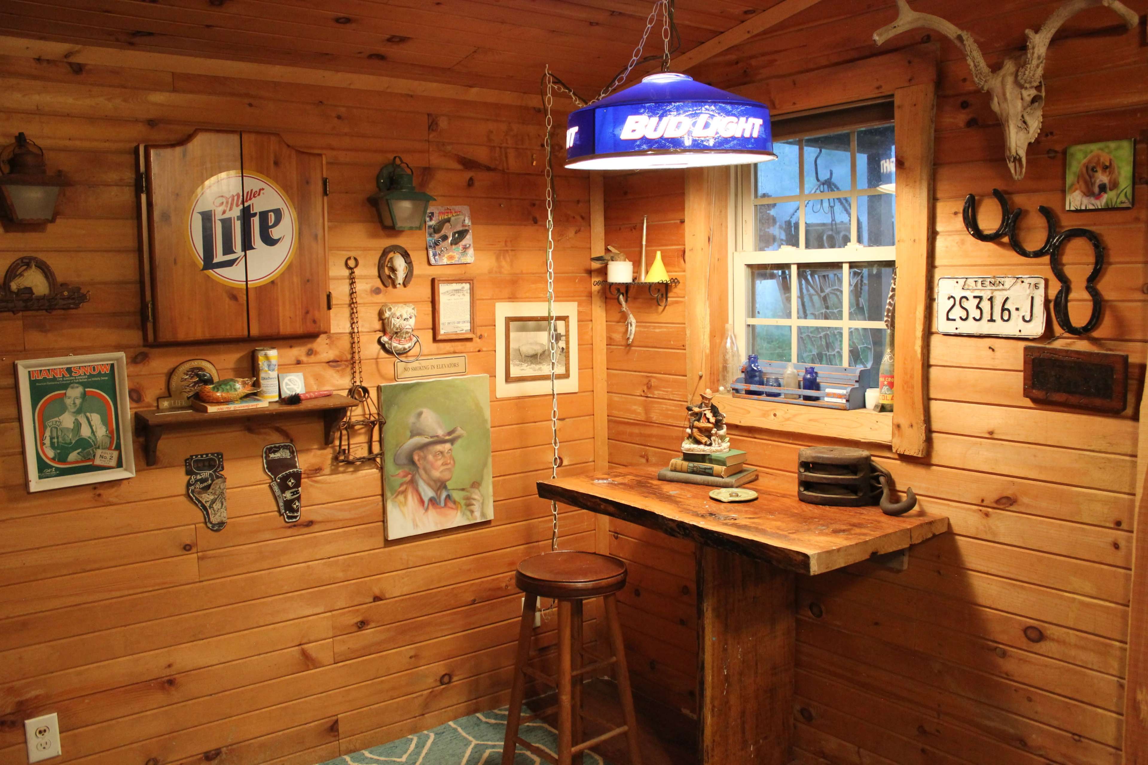 The image shows a rustic room with wooden walls adorned with various vintage decorations, including paintings and signs, and a wooden table with a barstool.