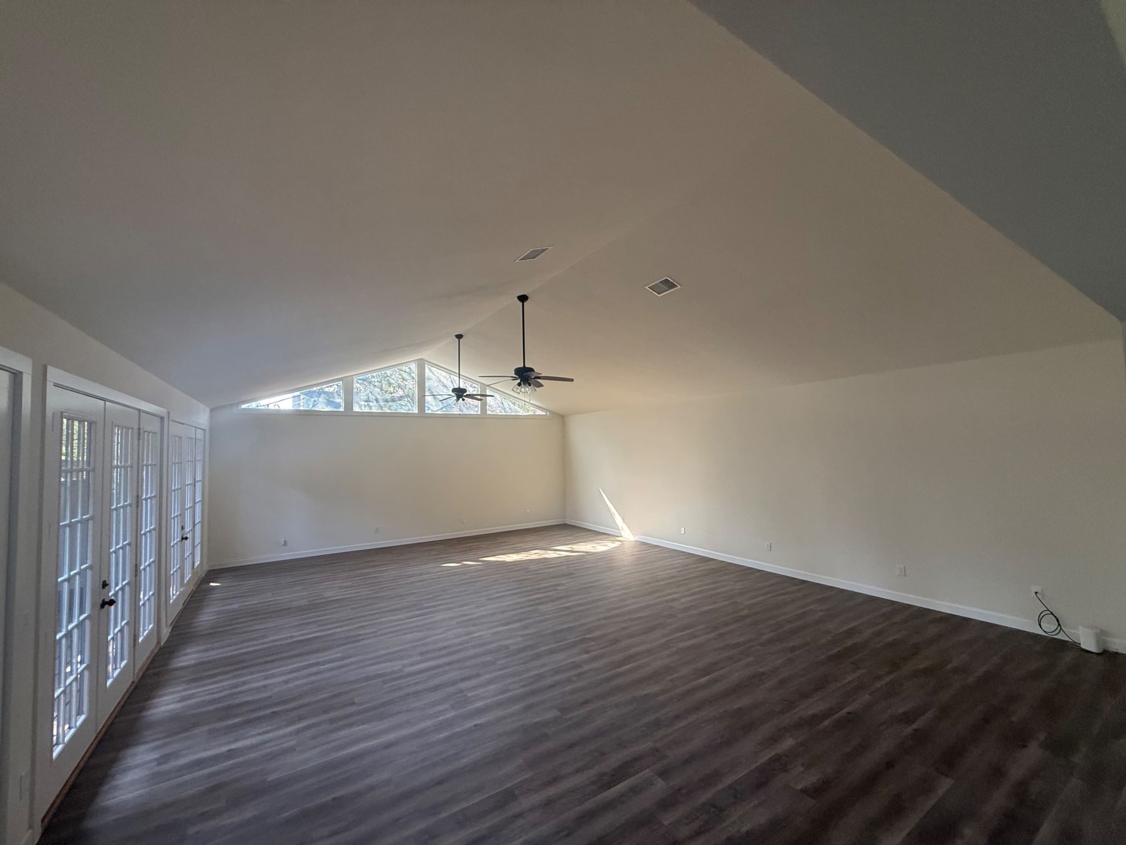 The image shows a spacious, empty room with high ceilings, large windows letting in natural light, and wooden flooring.
