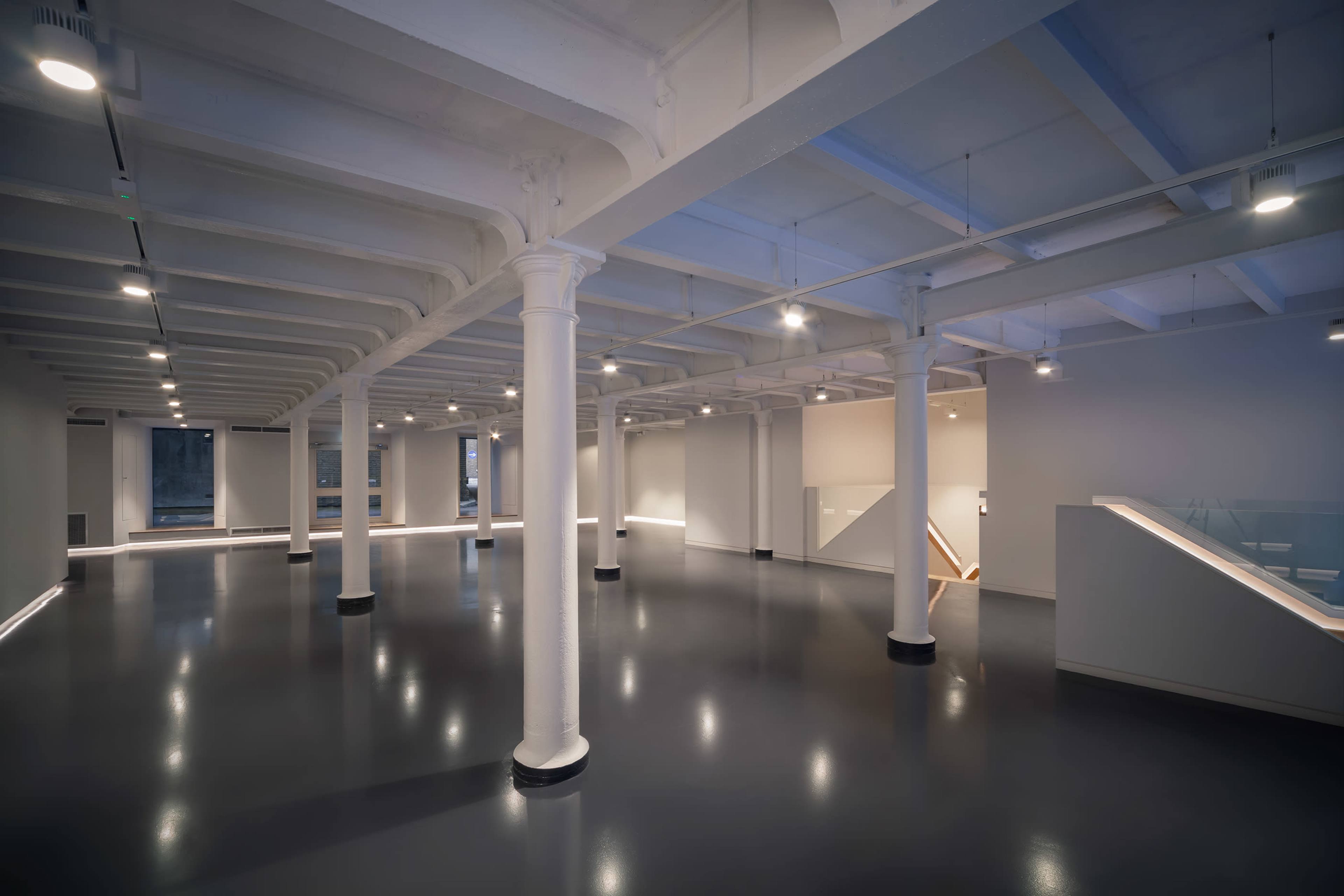 A spacious, modern interior featuring high ceilings, exposed beams, and polished flooring, illuminated by overhead lights.