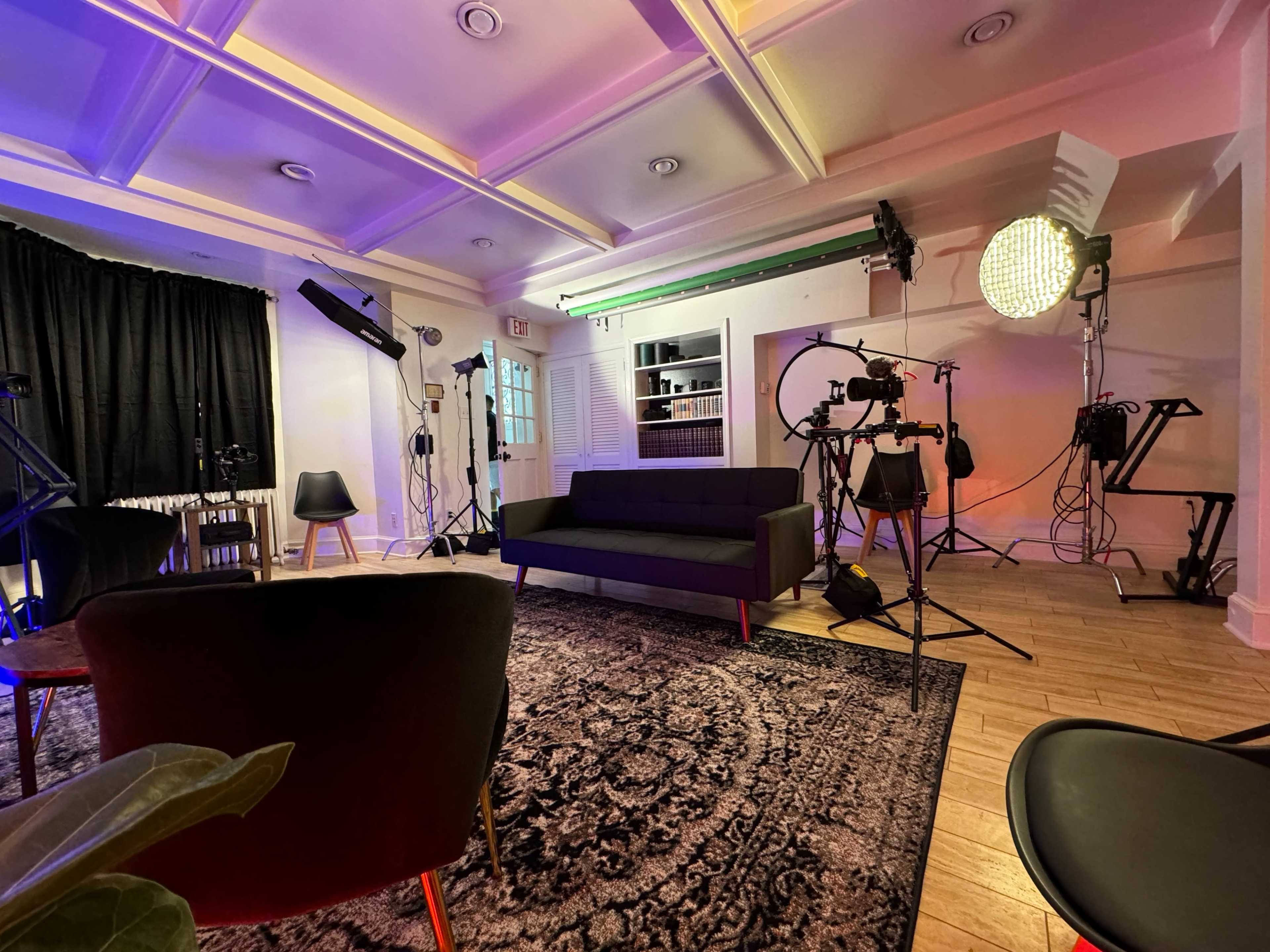 A modern studio space with a dark couch, various lighting equipment, and three chairs set on a patterned rug.