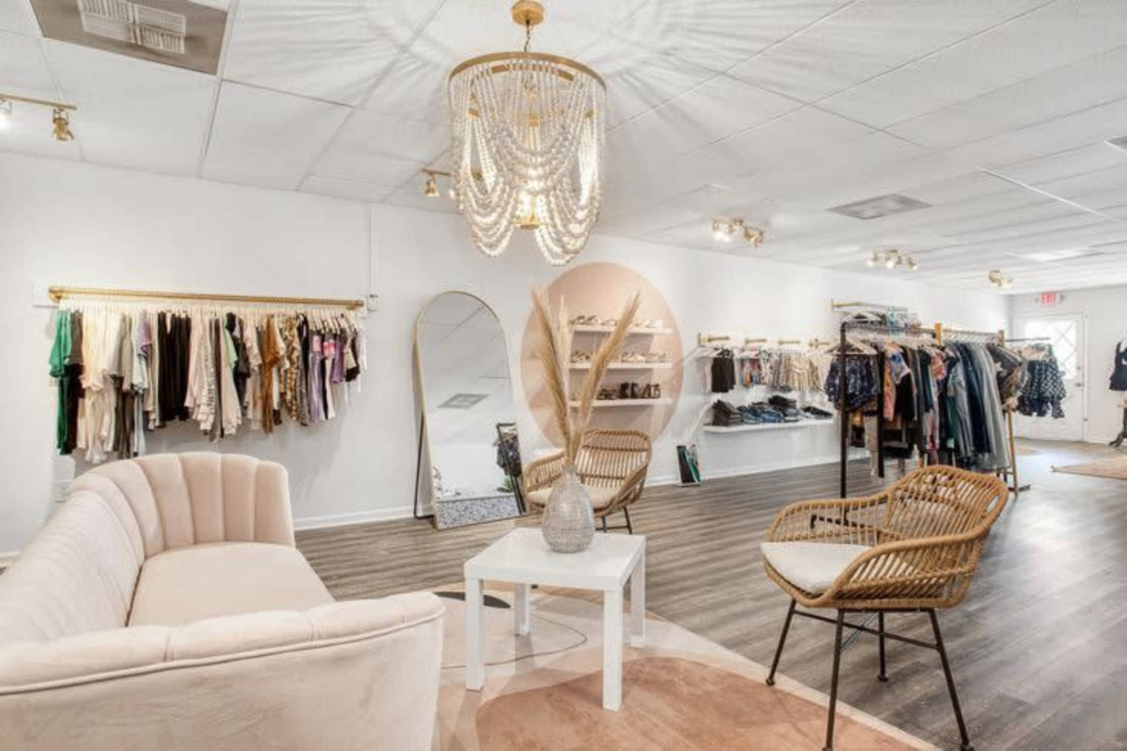 The image shows a clothing boutique featuring racks of apparel, a mirror, and seating arrangements with decorative elements.
