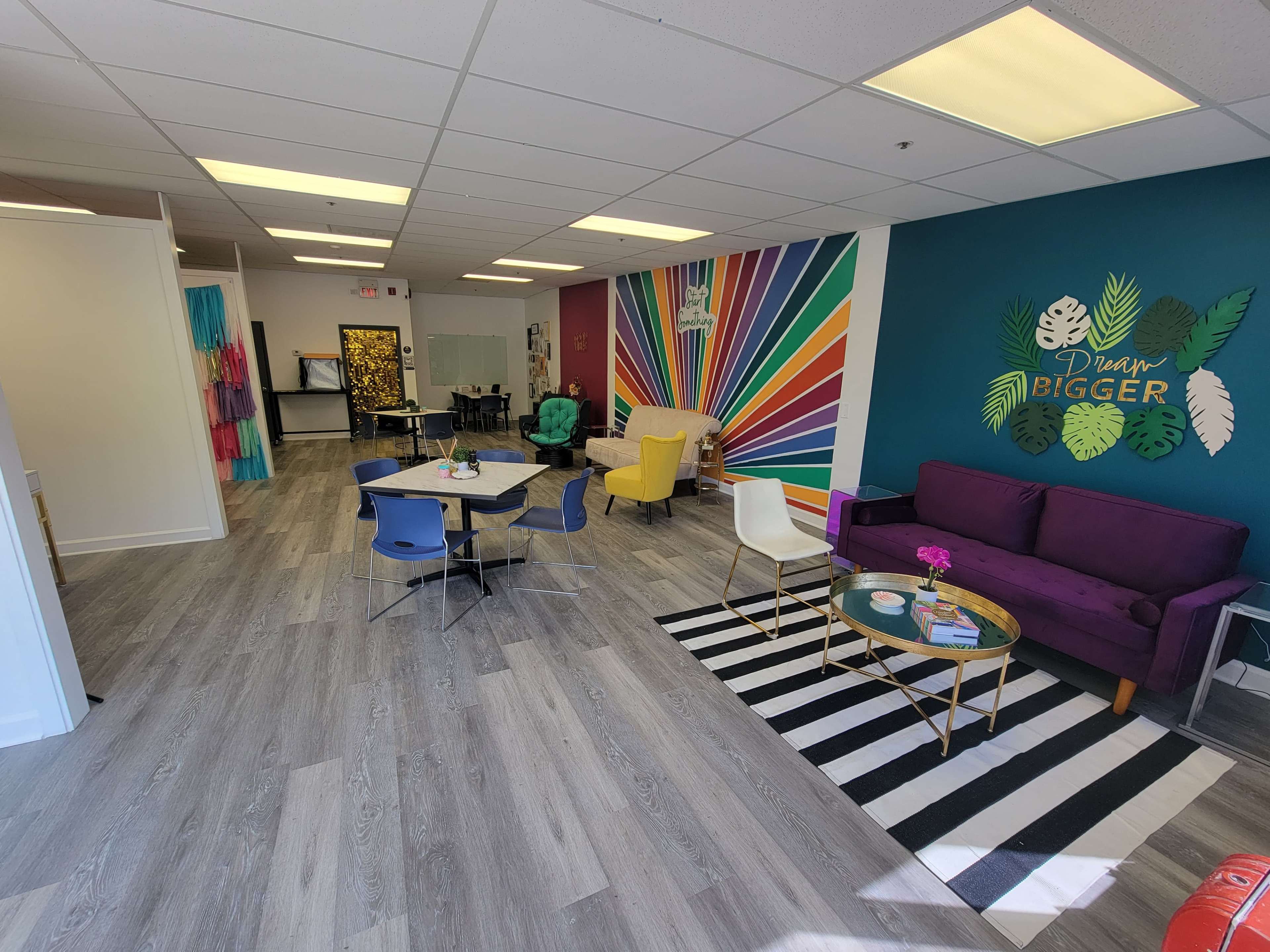 A brightly colored, modern open space featuring a seating area with a purple sofa, tables, and vibrant wall art.