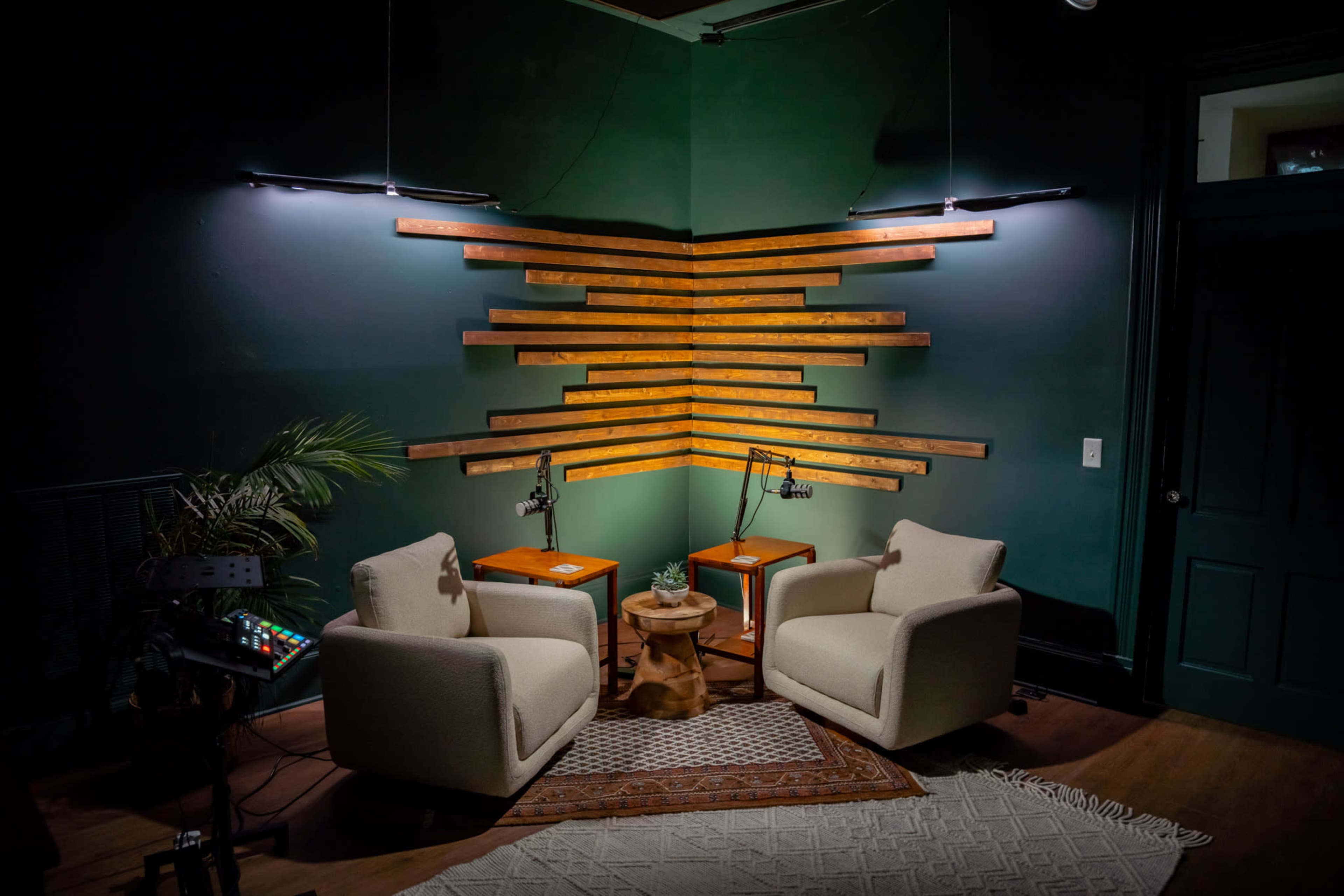 The image shows a cozy corner with two upholstered chairs, a small table, and decorative wooden wall panels illuminated by pendant lights.