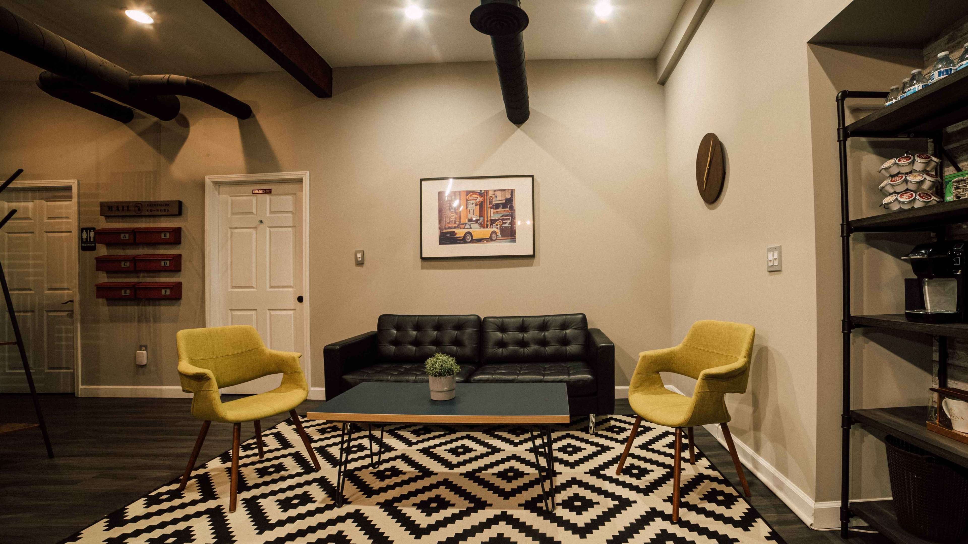 A modern sitting area with a black couch, two yellow chairs, a coffee table with a potted plant, and a geometric patterned rug.