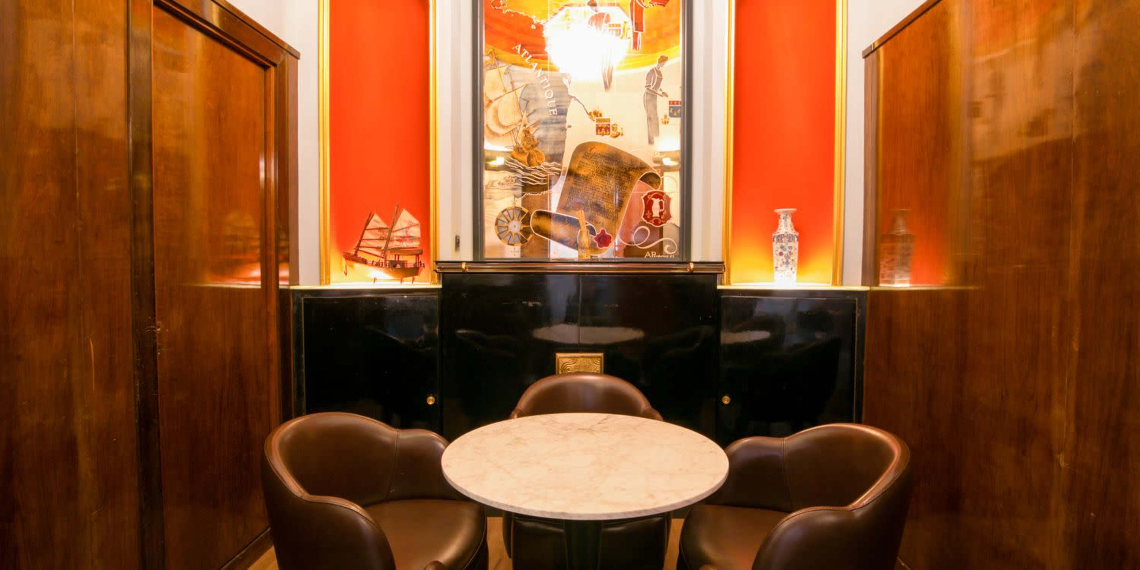 A small round marble table is surrounded by two dark leather chairs in a room with red walls and framed artwork.