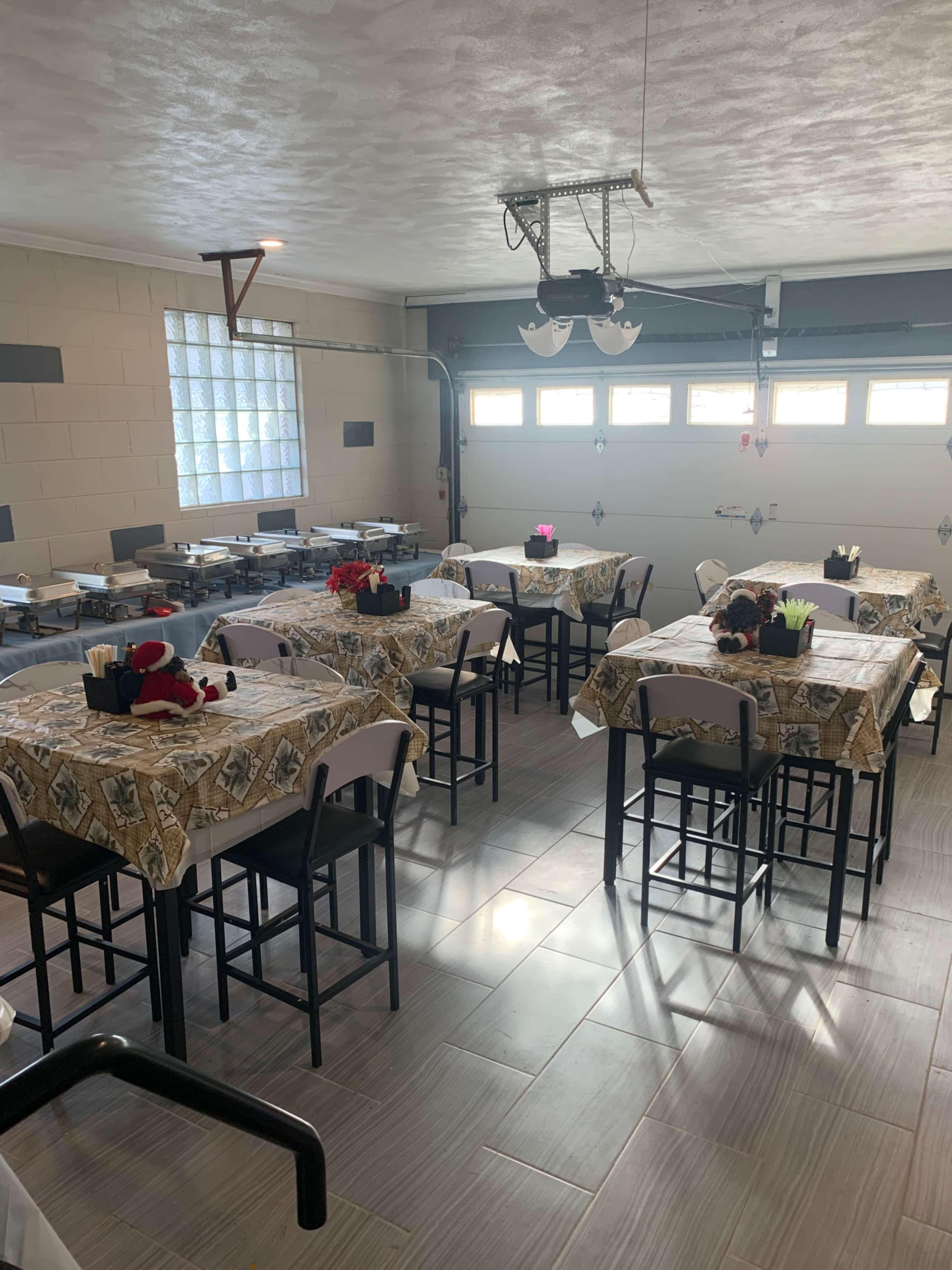 The image shows a neatly arranged indoor dining area with several tables covered in patterned tablecloths and decorated with small potted plants.