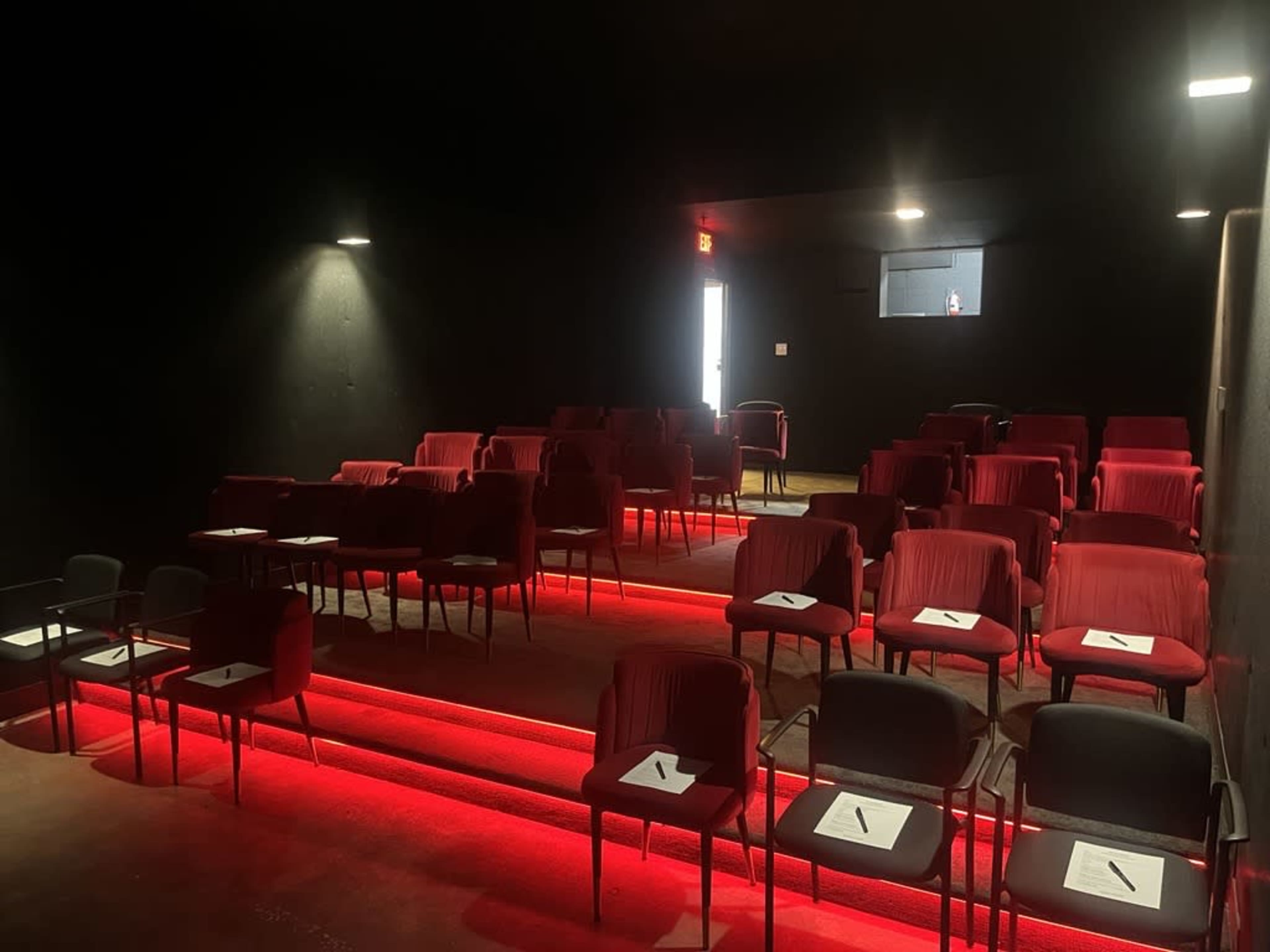The image shows an empty black-box theater with red seating and illuminated steps.