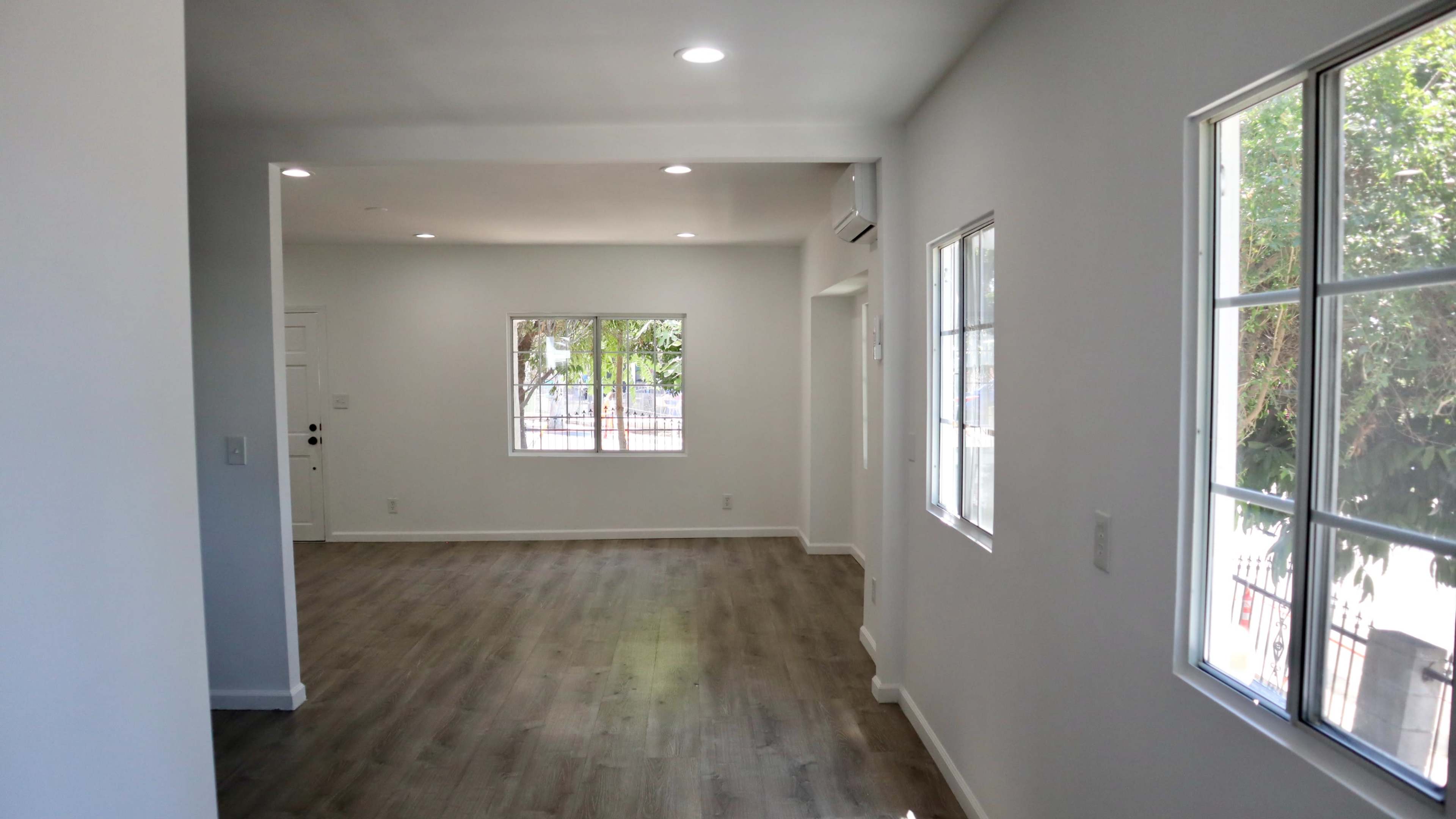 A spacious interior room with light-colored walls, wood-like flooring, and multiple windows allowing natural light to enter.