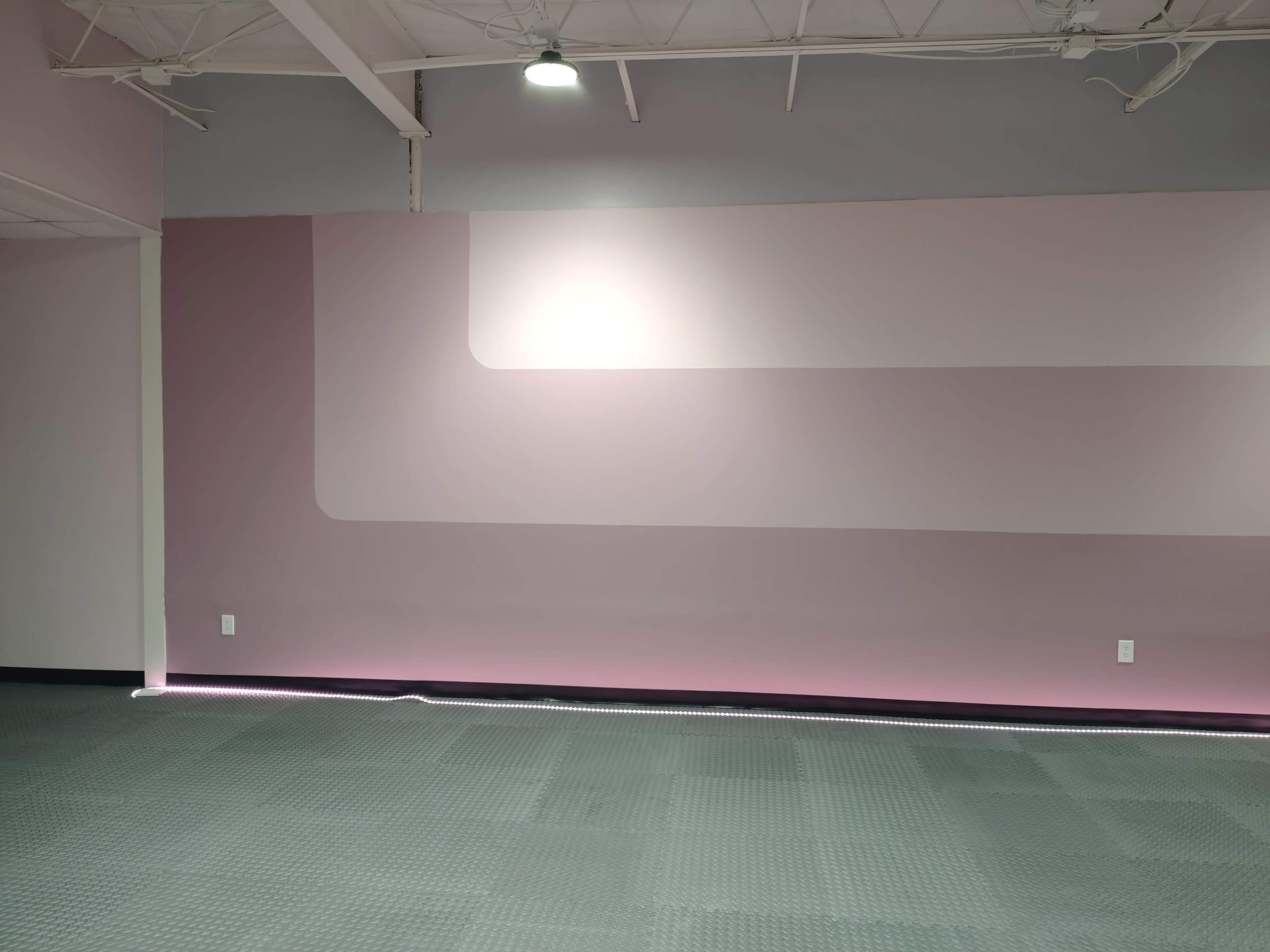 The image shows an empty room with a textured gray floor and a wall painted in gradient shades of pink.