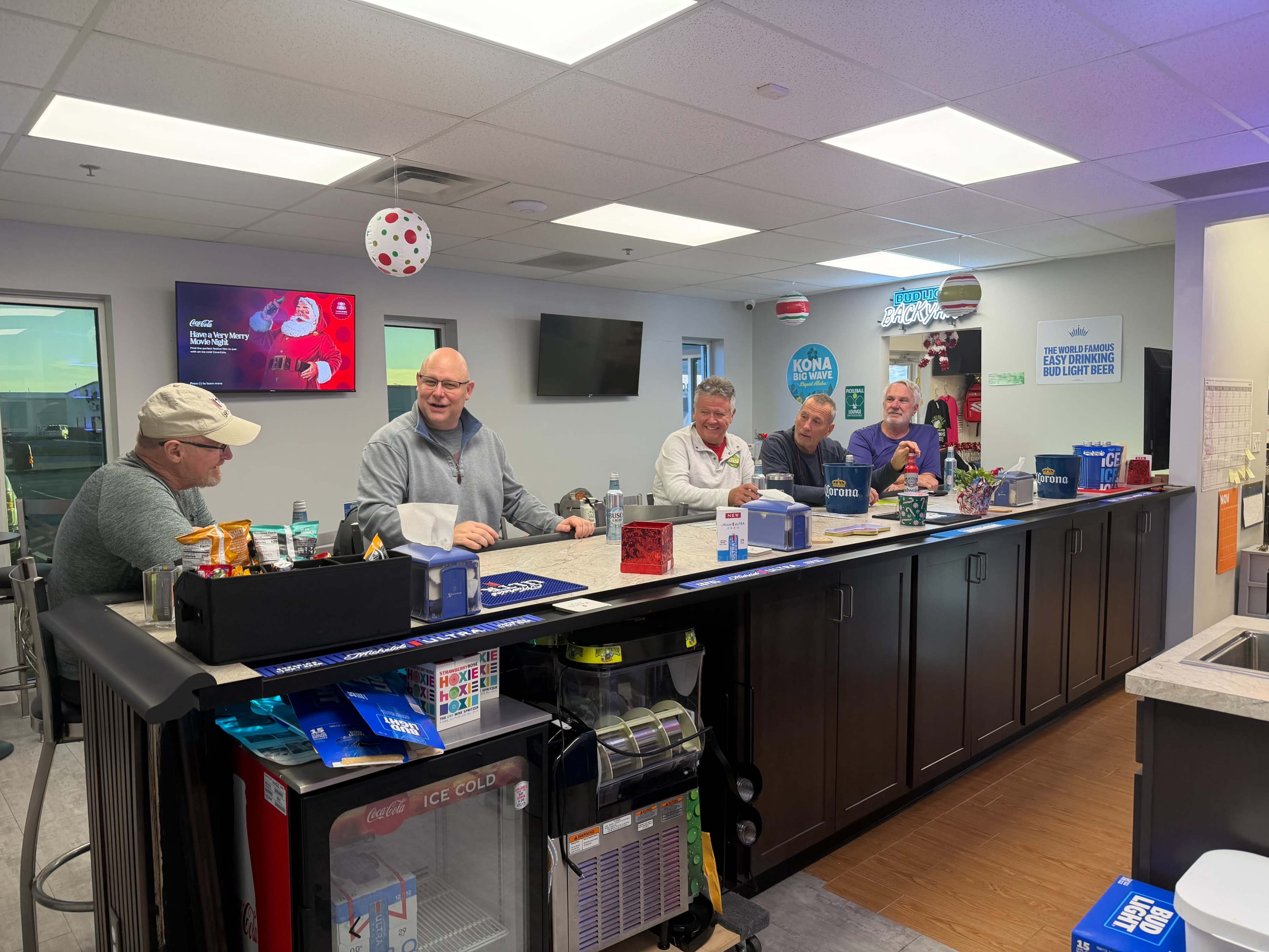 A group of five people are seated at a bar-style counter in a bright interior space, engaged in conversation.