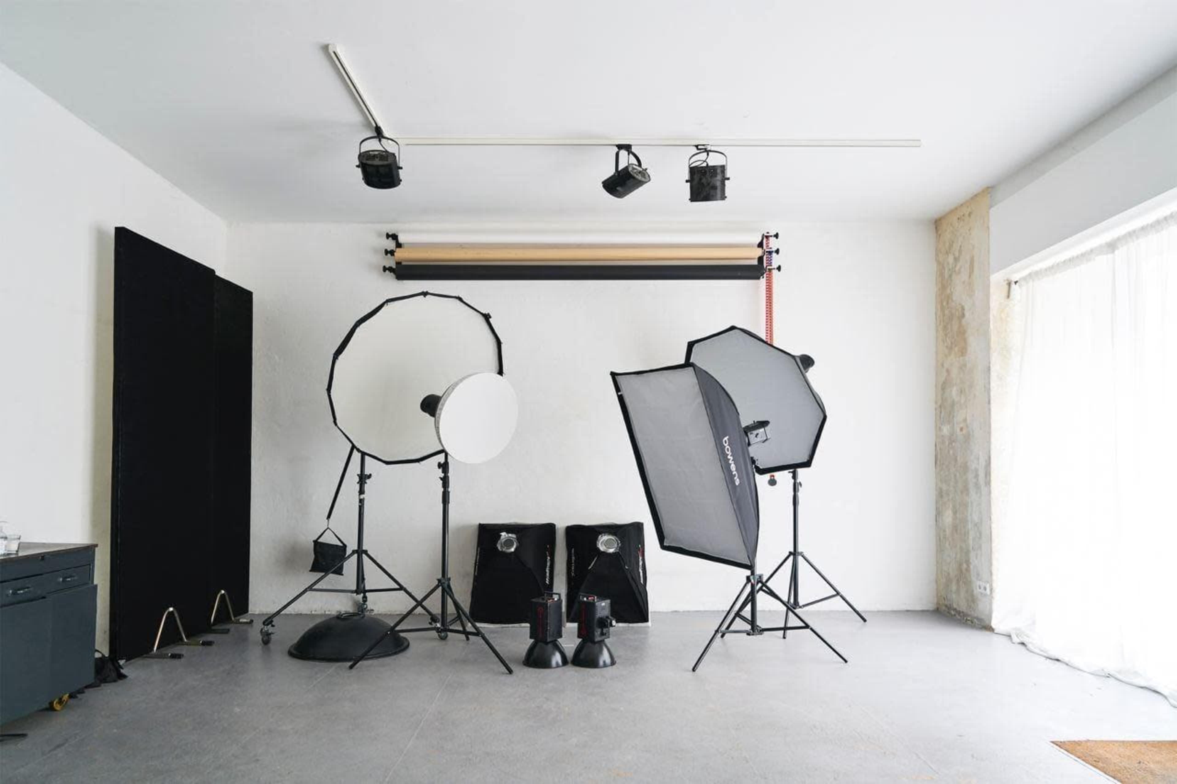 A photography studio is set up with various lighting equipment, including softboxes, reflectors, and background rolls.