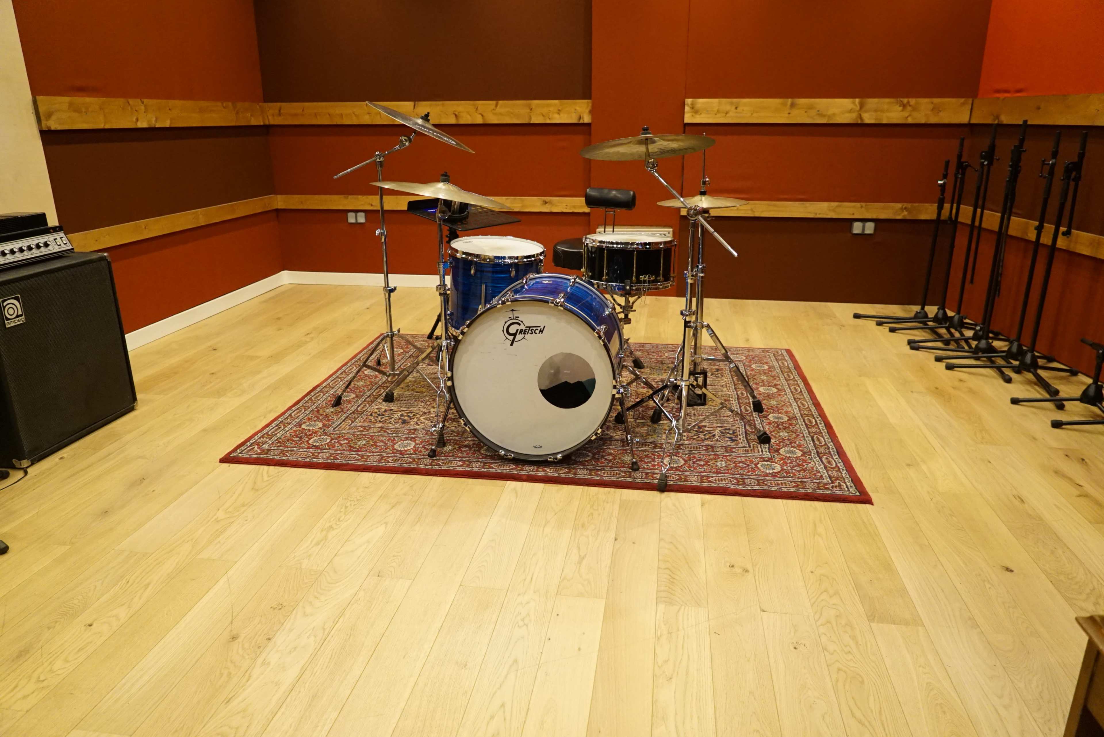 A drum set is positioned on a patterned rug within a soundproof room featuring wooden wall panels and polished wooden flooring.
