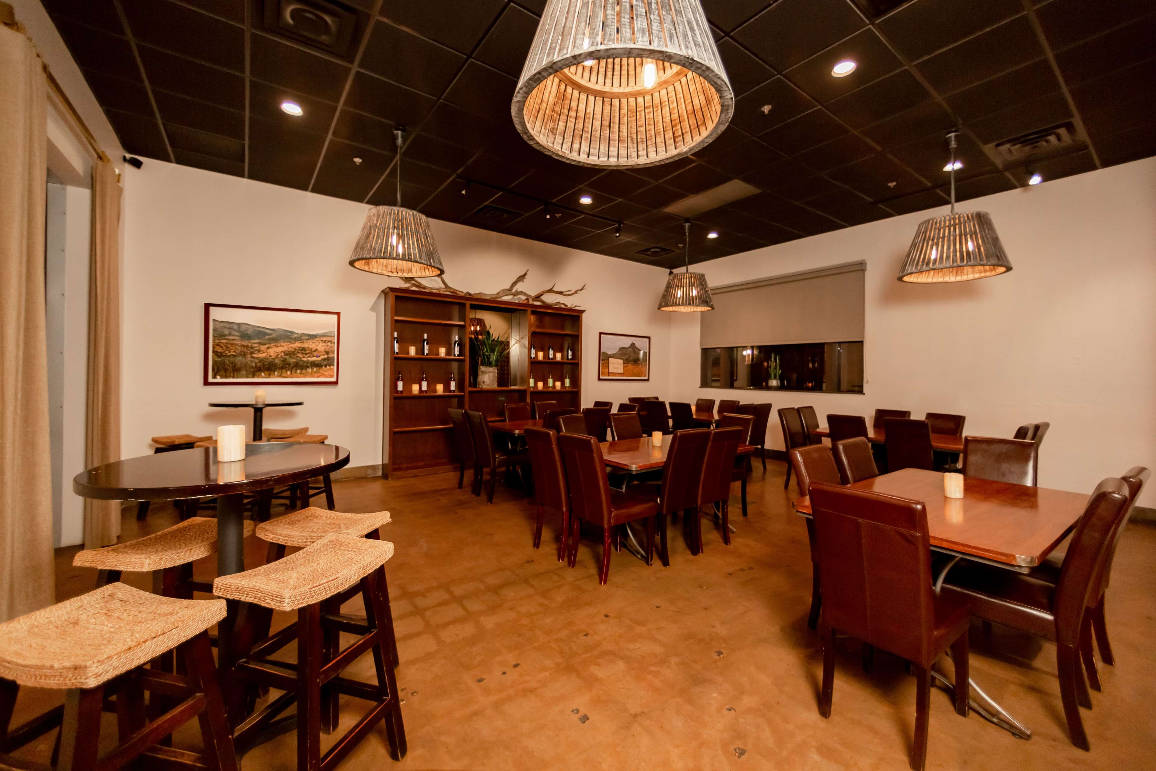 A dining area with wooden tables and chairs, surrounded by decorative light fixtures and a bookshelf against one wall.