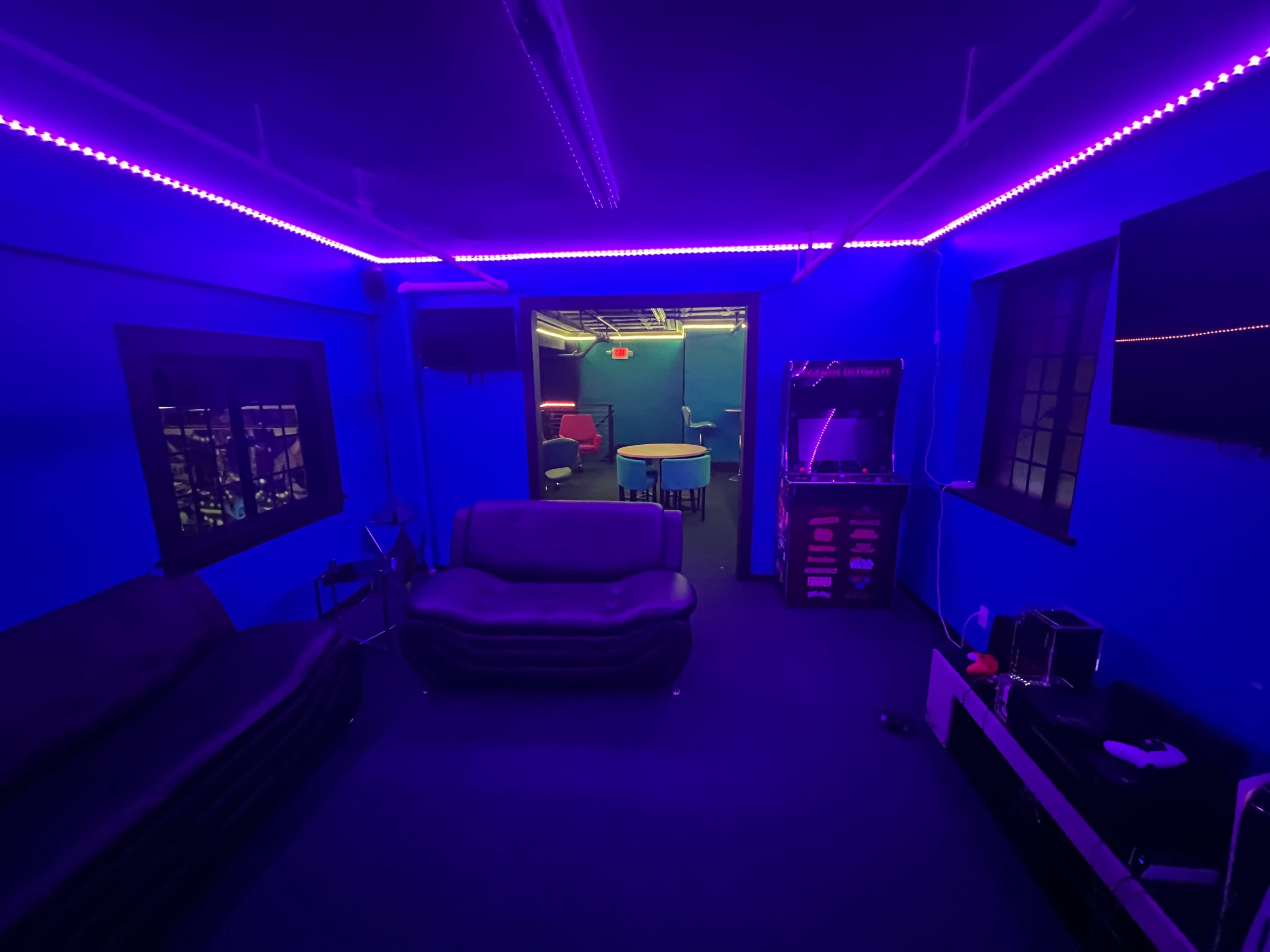 A dimly lit room with blue walls features a black couch and neon purple lighting.