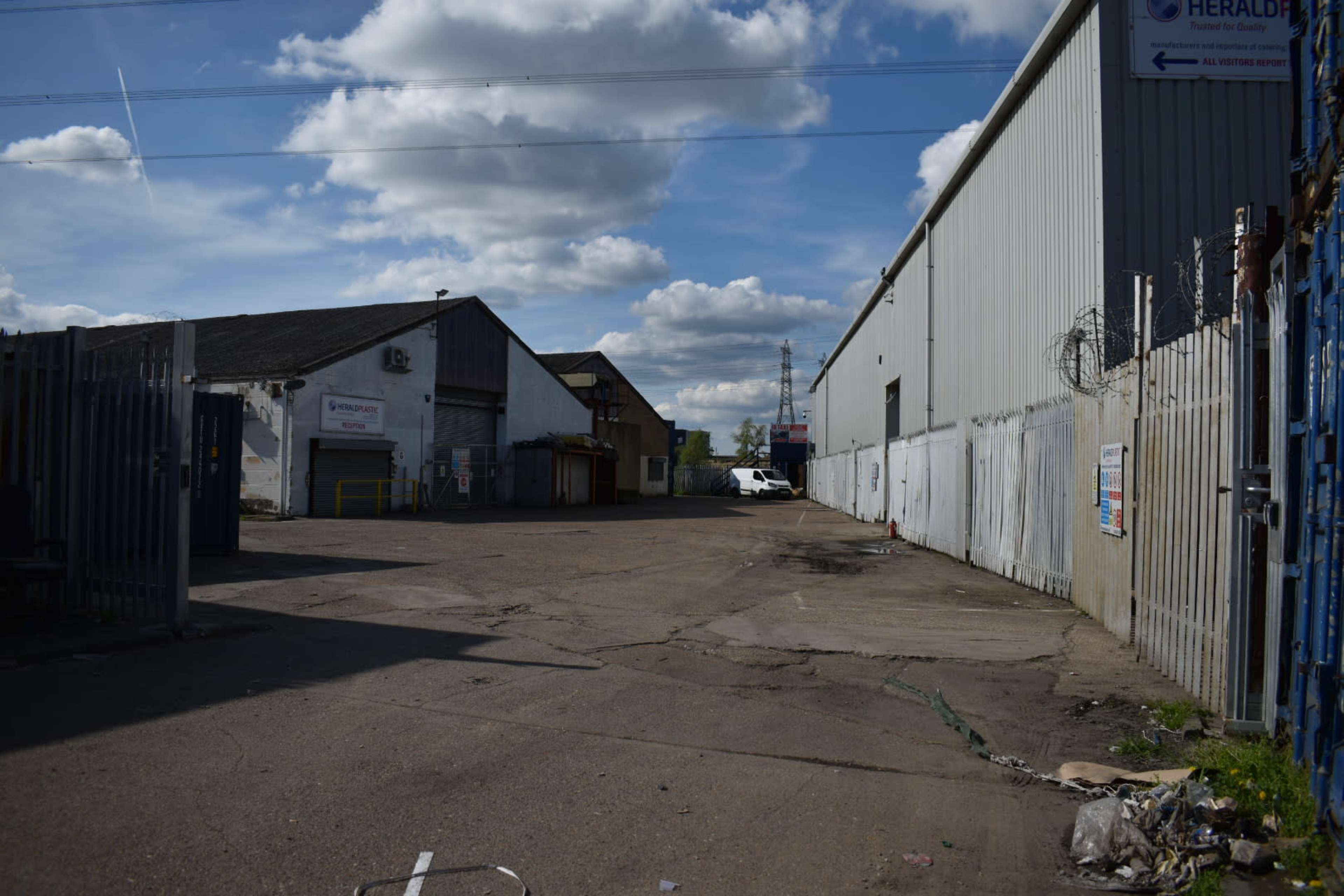 The image shows a wide, empty industrial area with buildings on either side and a clear sky overhead.