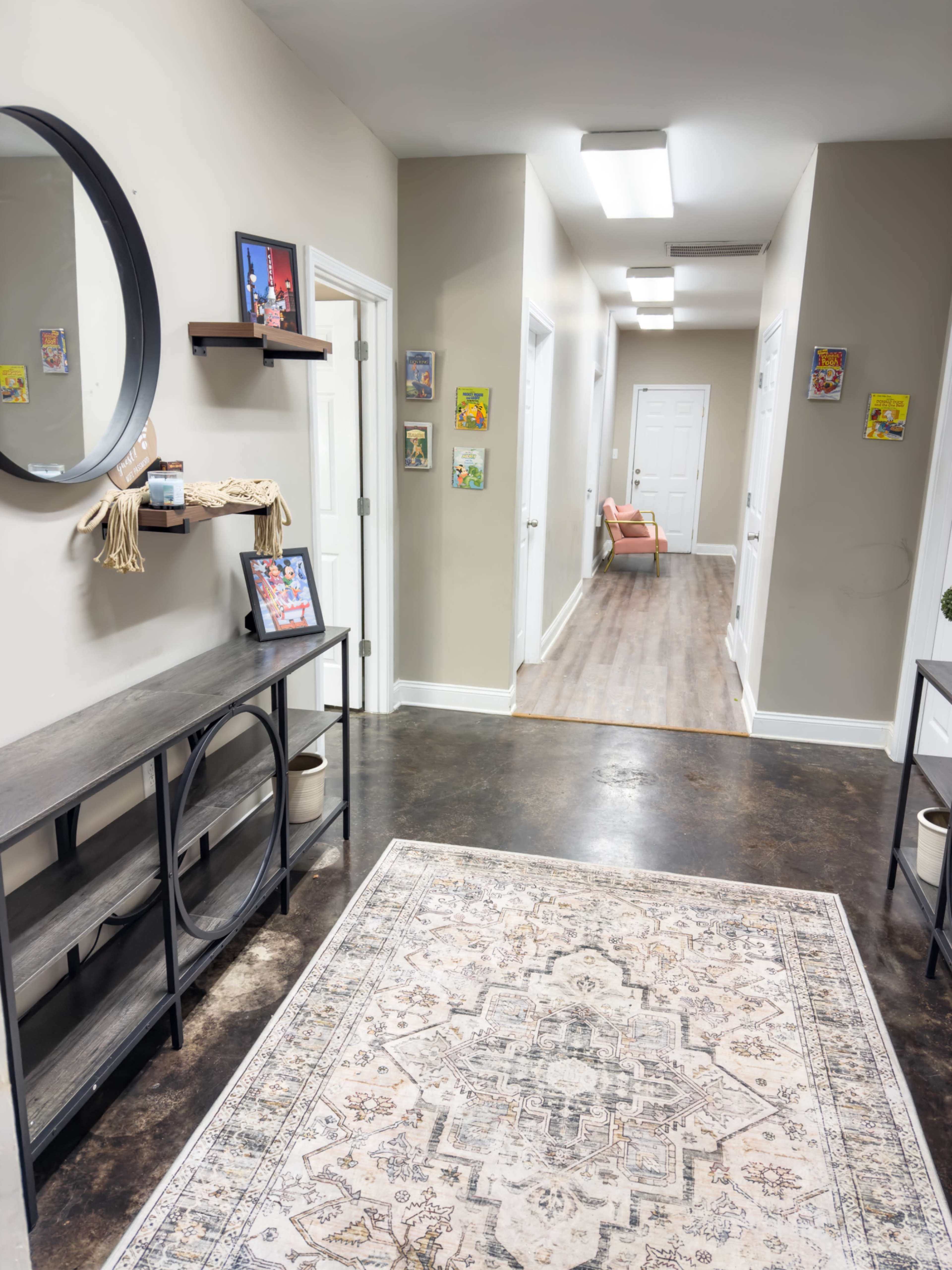 A hallway features a decorative rug, a round mirror, wall art, and a seating area at the far end.