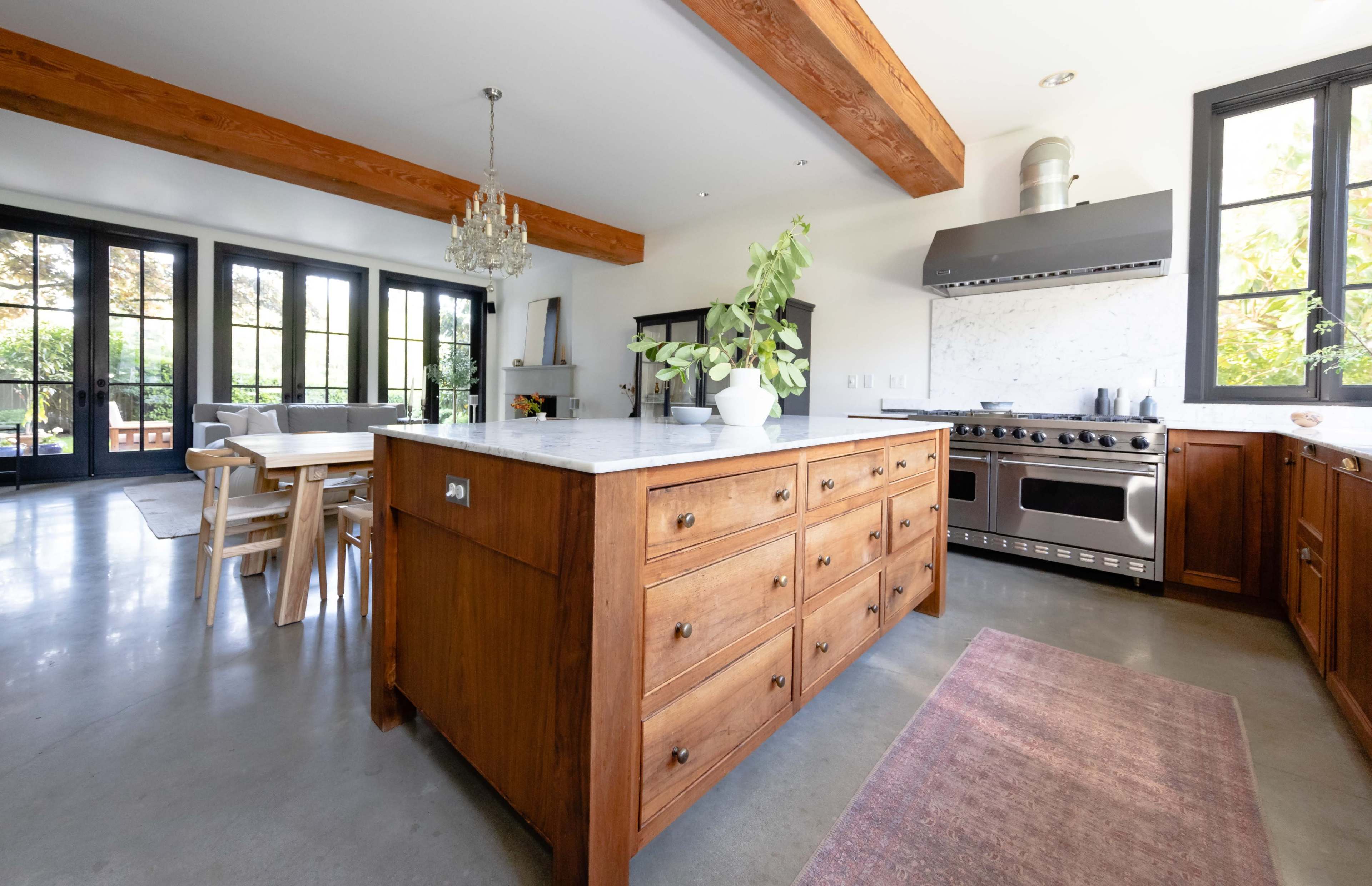 A modern kitchen with a large wooden island, stainless steel appliances, and large windows that provide natural light.