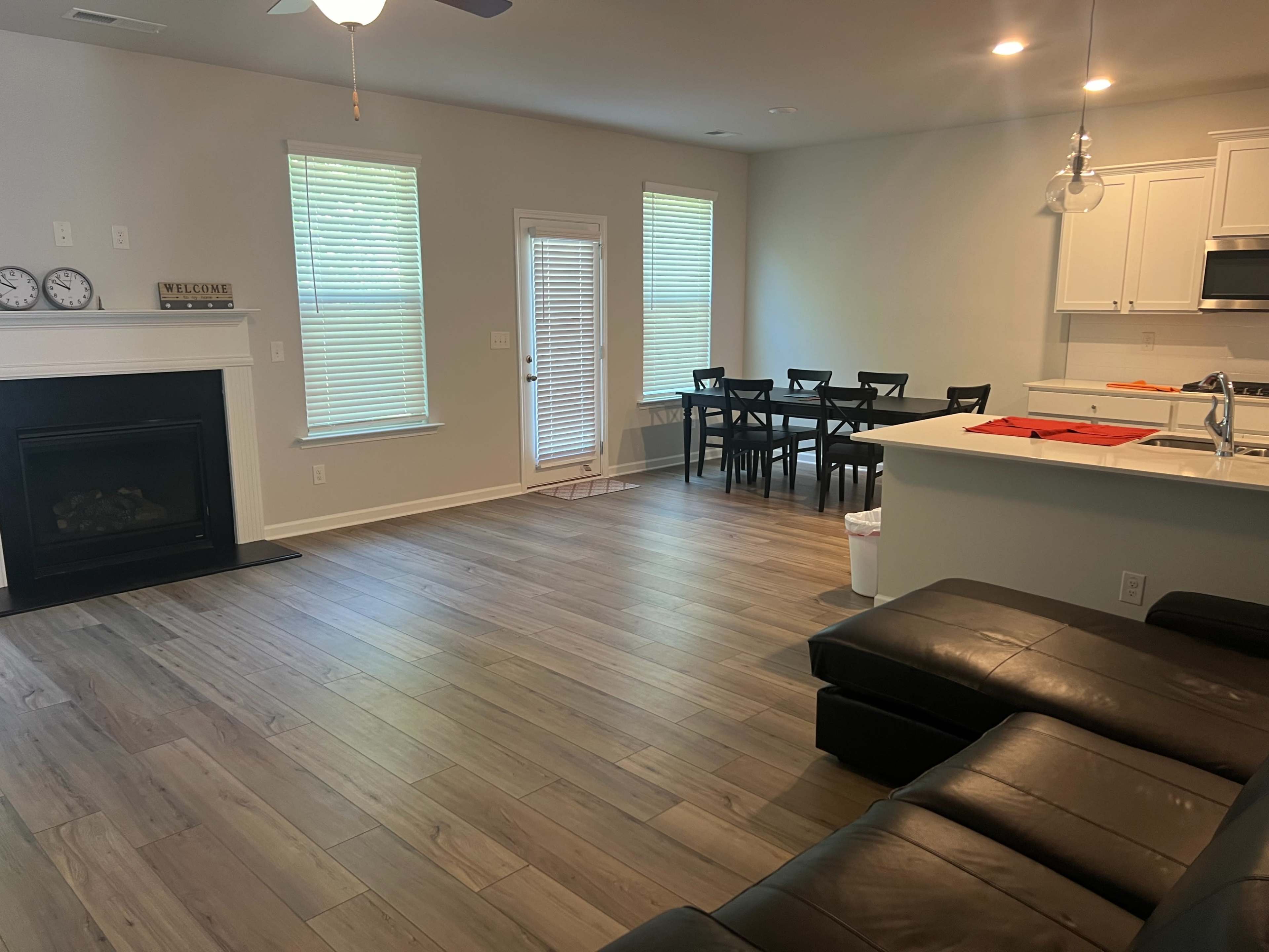 A spacious living area with a seating arrangement, dining table, and a kitchen space featuring light-colored cabinetry.