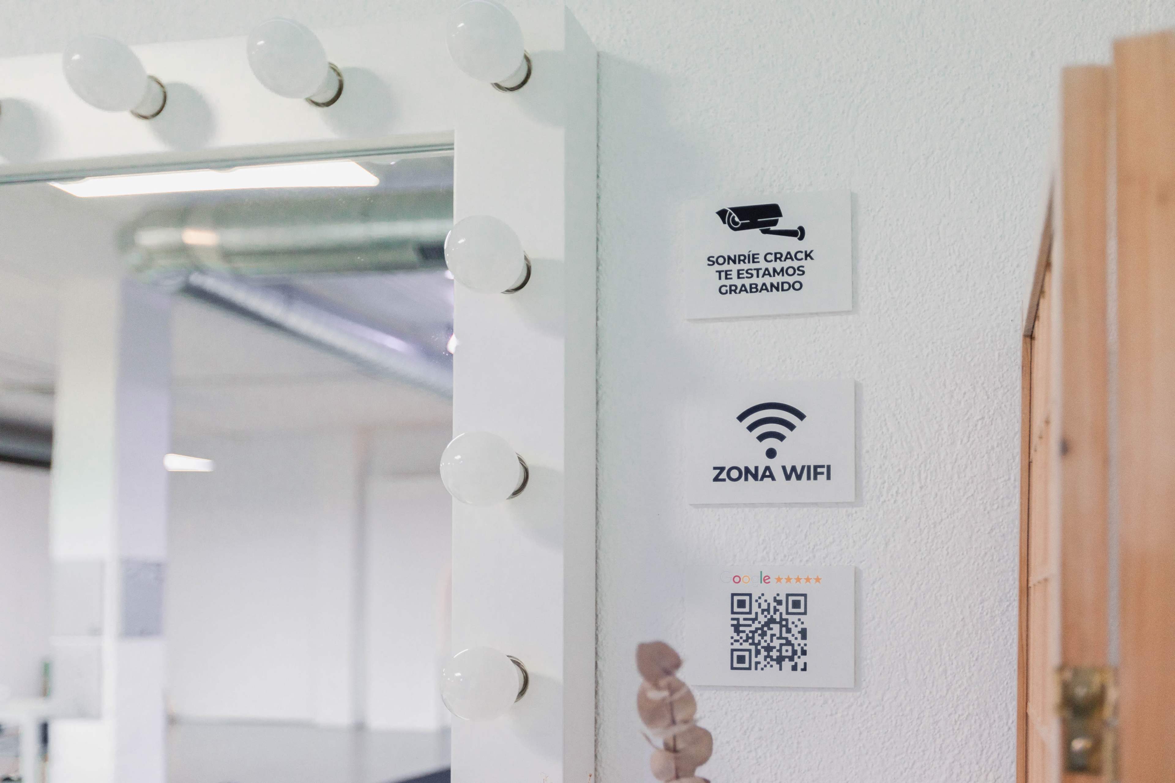 A wall-mounted mirror with bright bulbs, accompanied by signs indicating a recording notice and Wi-Fi zone.