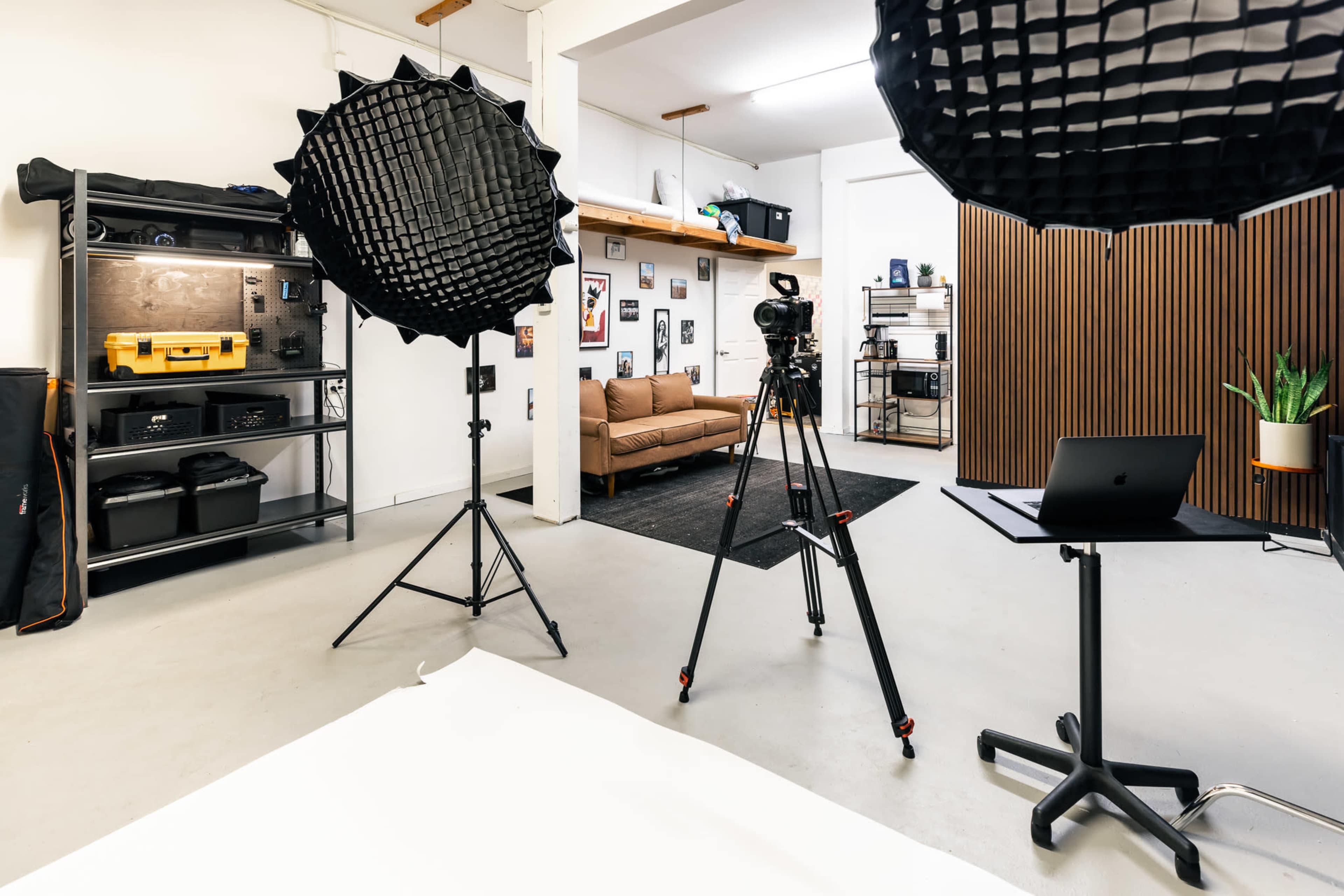A photography studio equipped with softbox lights, a camera on a tripod, a computer on a stand, and a cozy seating area in the background.