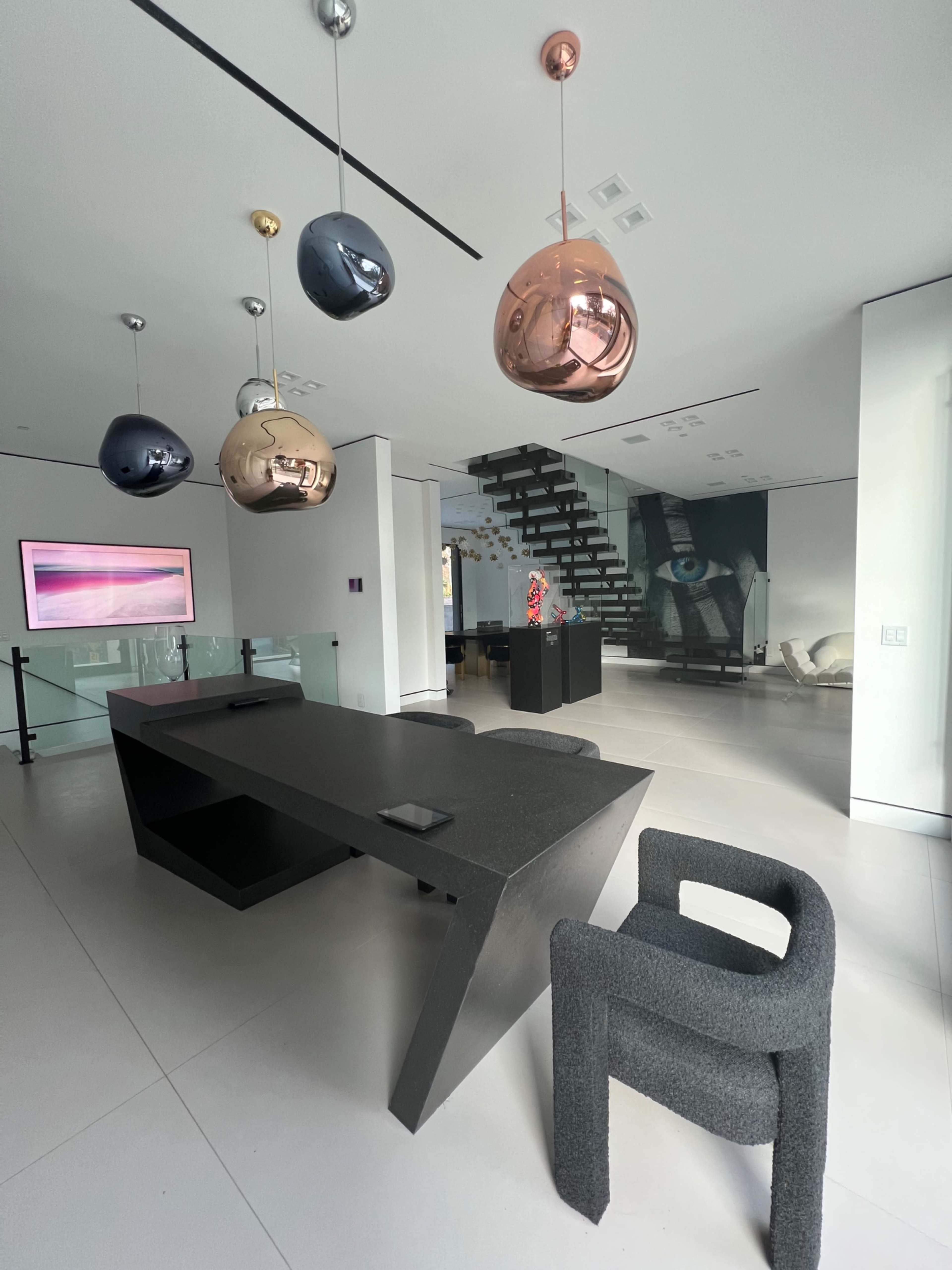 A modern interior space with a black dining table, colorful pendant lights, and a minimalist staircase in the background.